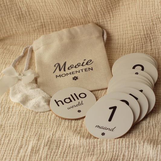 Set ronde baby mijlpaalschijfjes met linnen zakje op een beige mousseline doek.