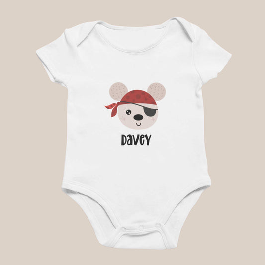 Wit babyrompertje met een illustratie van een beer met een rode bandana en ooglapje en een naam eronder