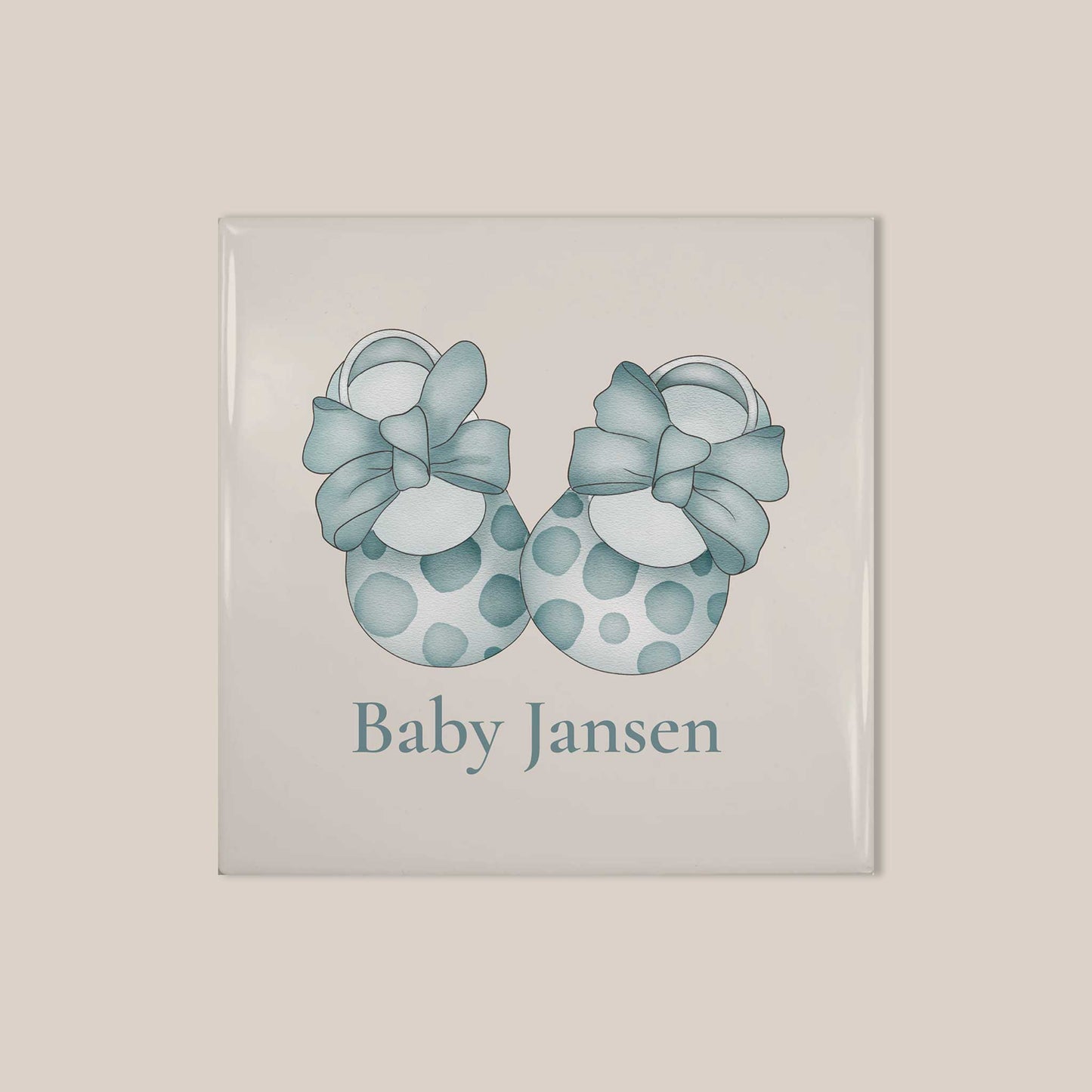 Vierkant keramisch baby tegeltje met illustratie van blauwe babyschoentjes met strikken en gepersonaliseerde naam Baby Jansen op lichte achtergrond.