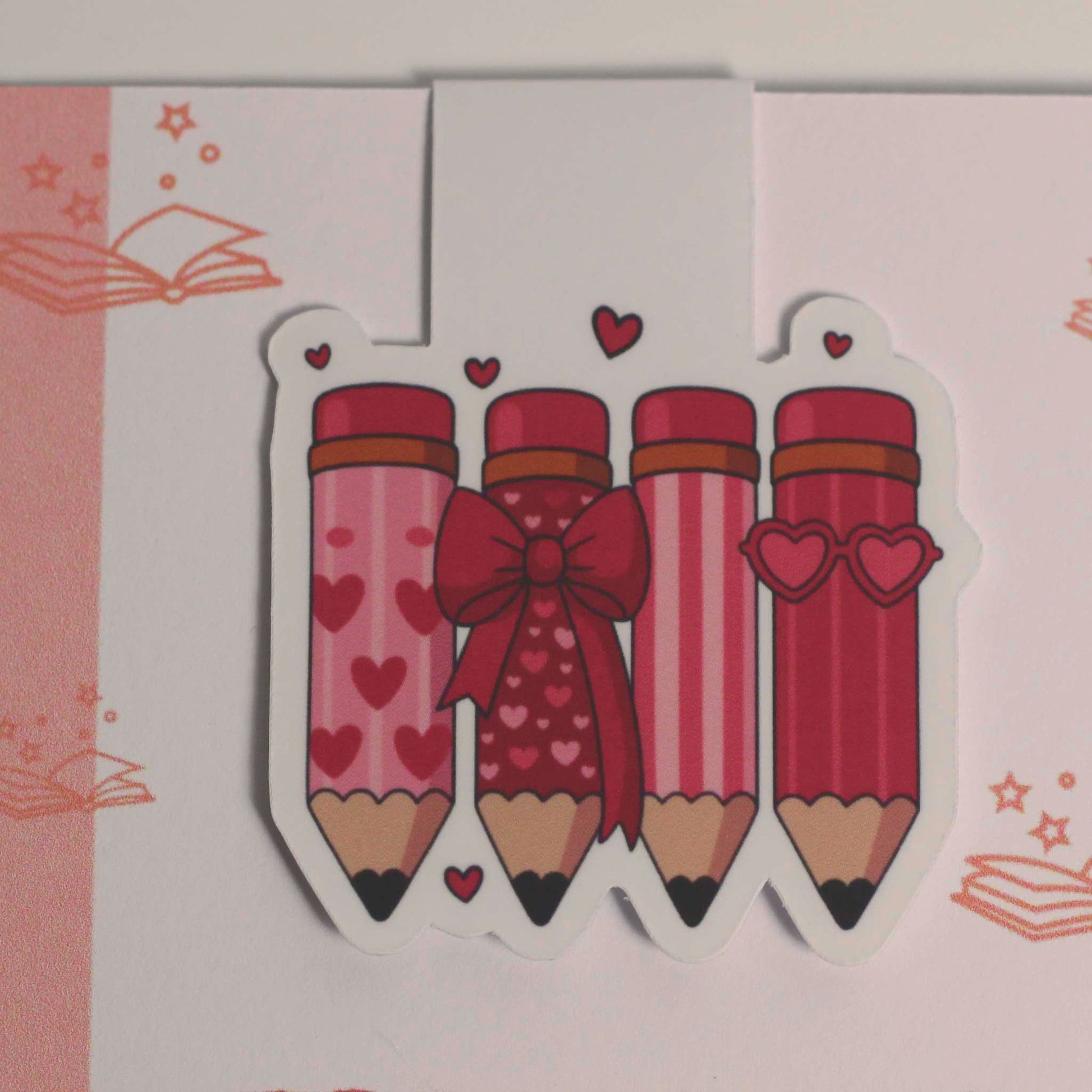 Detailfoto van een magnetische boekenlegger met vier roze potloden, hartjes en een rode strik op een lichte achtergrond