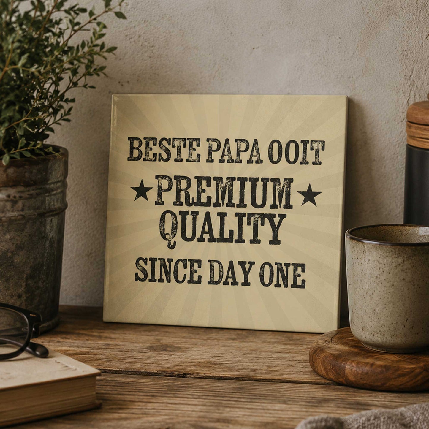 Vintage keramisch tegeltje met de tekst “Beste Papa Ooit Premium Quality Since Day One” op warme houten tafel met mok en planten