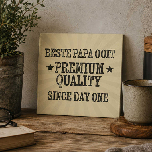 Vintage keramisch tegeltje met de tekst “Beste Papa Ooit Premium Quality Since Day One” op warme houten tafel met mok en planten