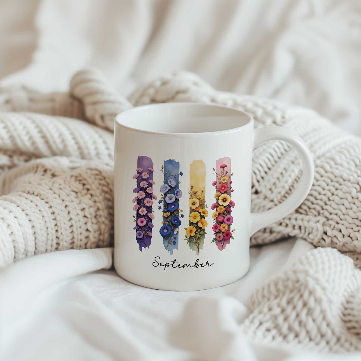 Keramische mok met de geboortebloemen aster en winde van september op een zachte gebreide beige deken.