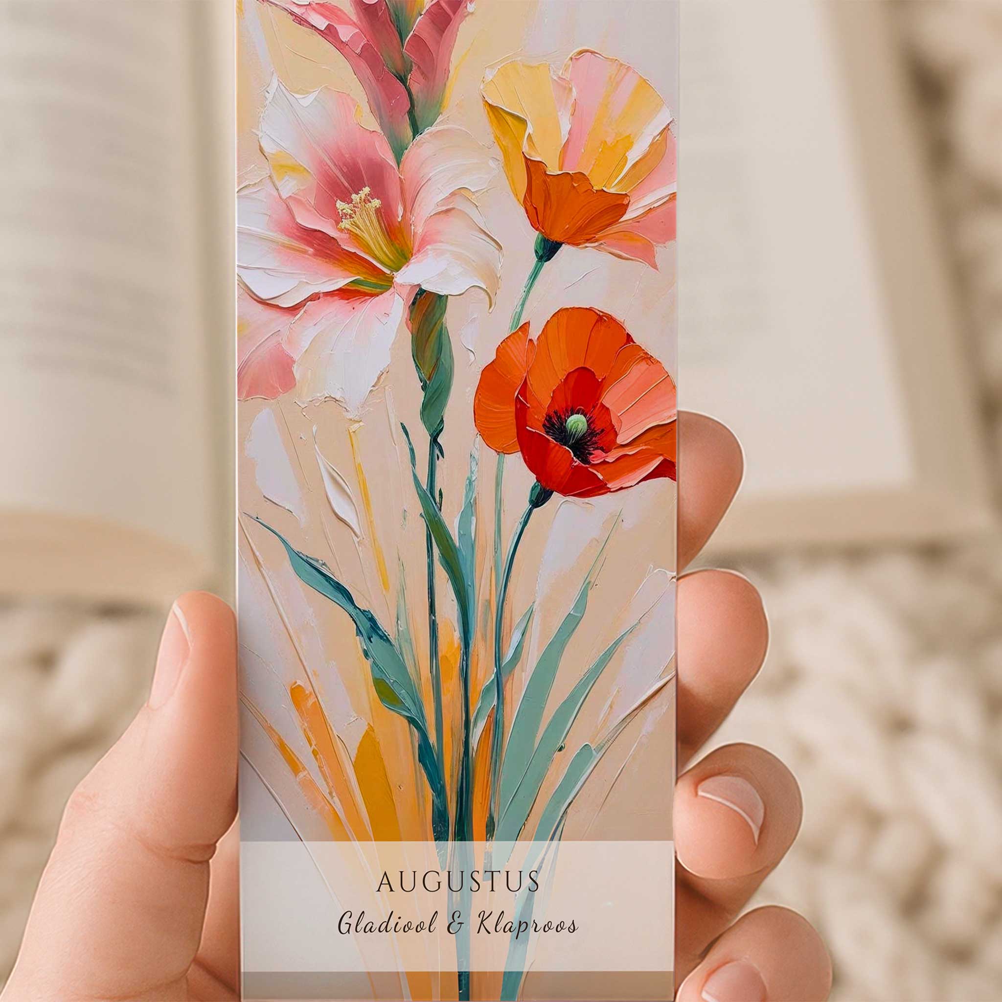 Close-up van een hand die een boekenlegger met de geboortebloemen van augustus vasthoudt. De kunstzinnige illustratie toont een gladiool en klaproos in zachte roze-, oranje- en roodtinten, met onderaan de tekst 'Augustus – Gladiool & Klaproos'.