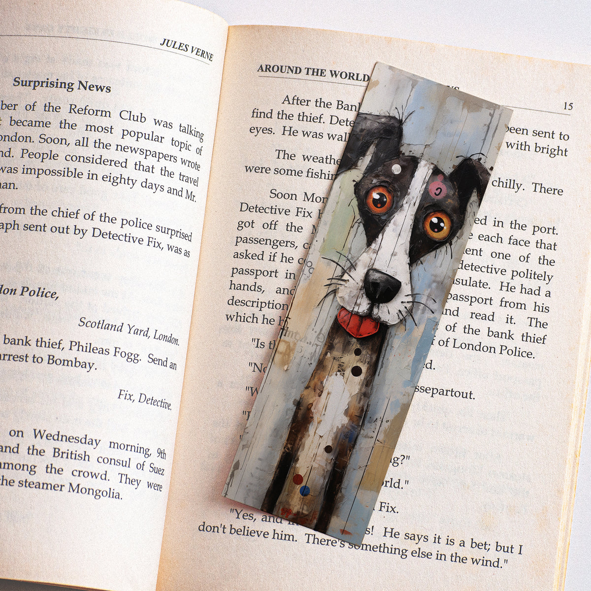 Boekenlegger met artistieke zwart-witte hond met flapoor en grote oranje ogen tussen de pagina's van een open boek.