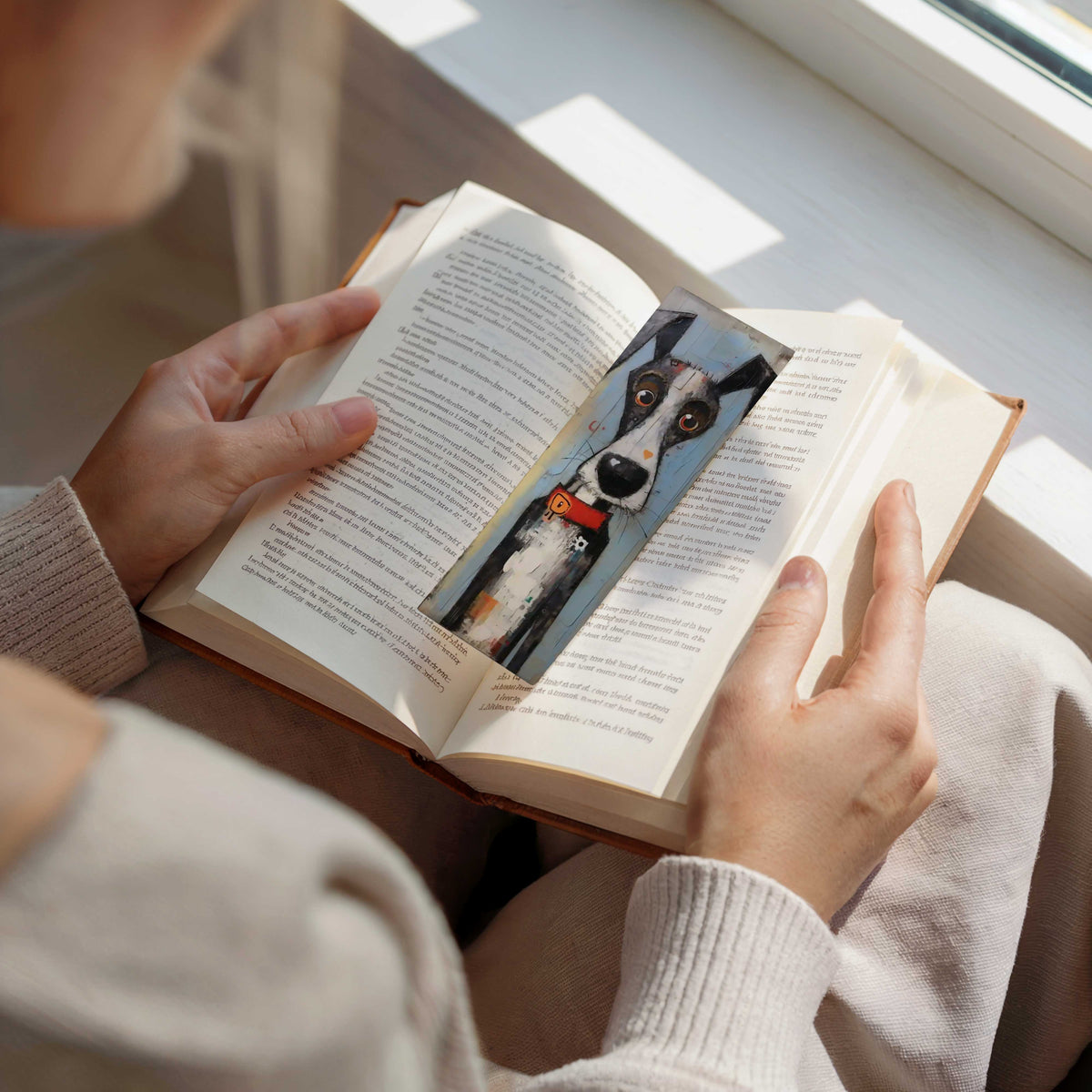 Persoon leest een open boek met een boekenlegger met zwart-witte hond en rode halsband tussen de pagina's.