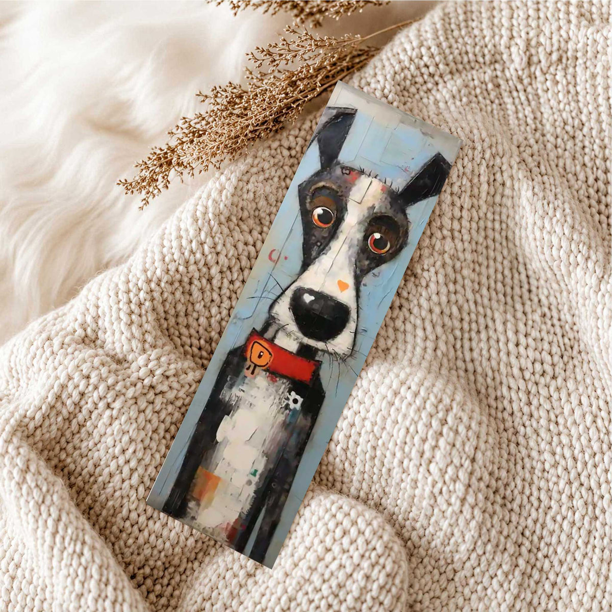 Boekenlegger met zwart-witte hond, grote ogen en rode halsband liggend op een zachte beige gebreide deken.