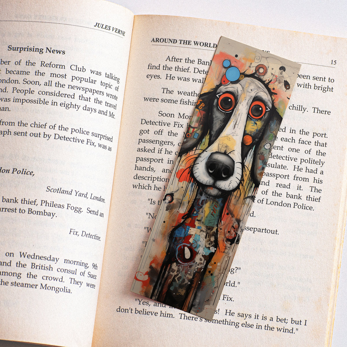 Boekenlegger met kleurrijke artistieke hond en grote rood-oranje ogen, liggend tussen de pagina's van een open boek.