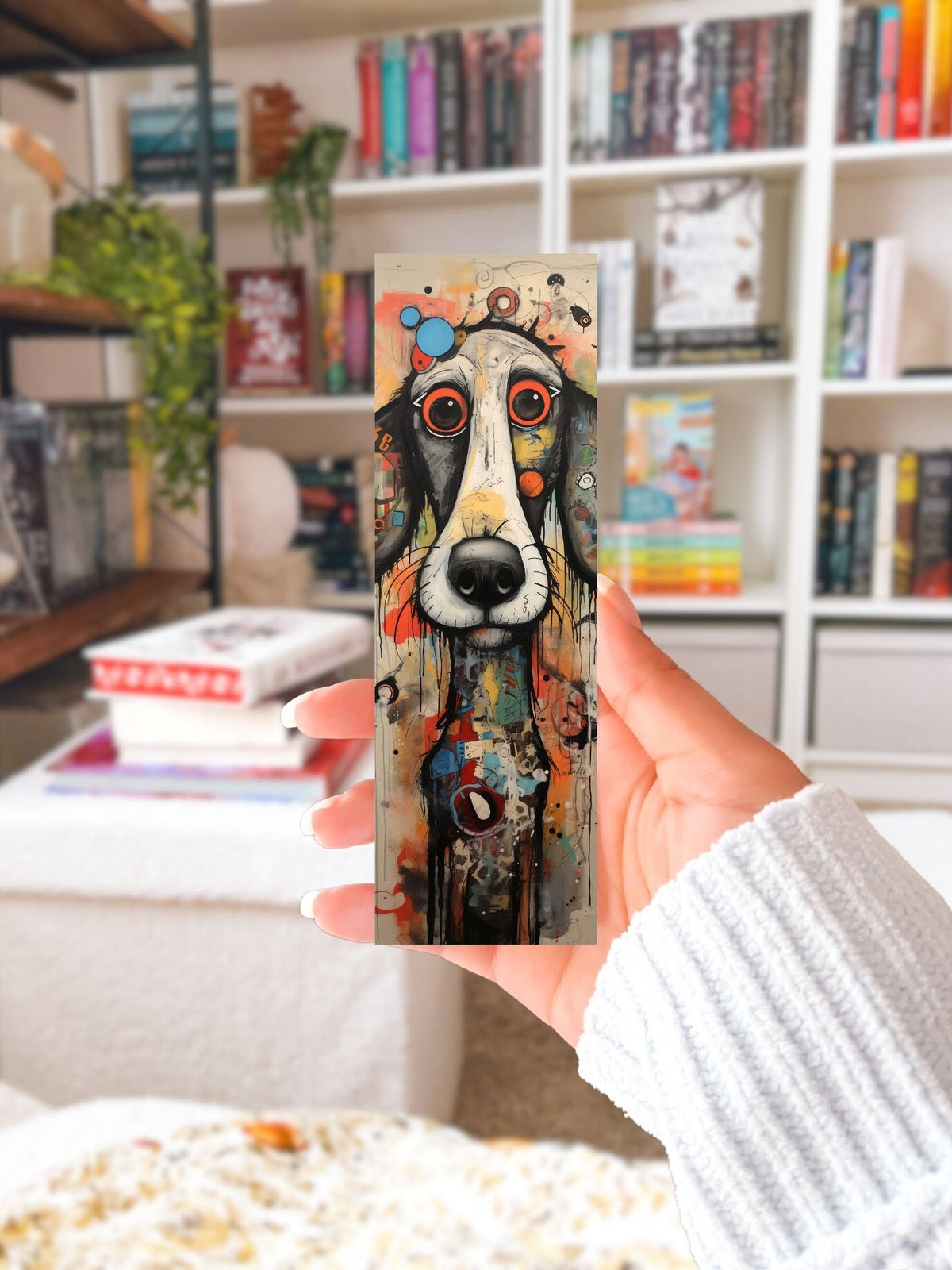 Hand houdt boekenlegger Hond Kunst vast met een langgerekte zwart-witte hond, grote ogen en kleurrijke abstracte accenten.