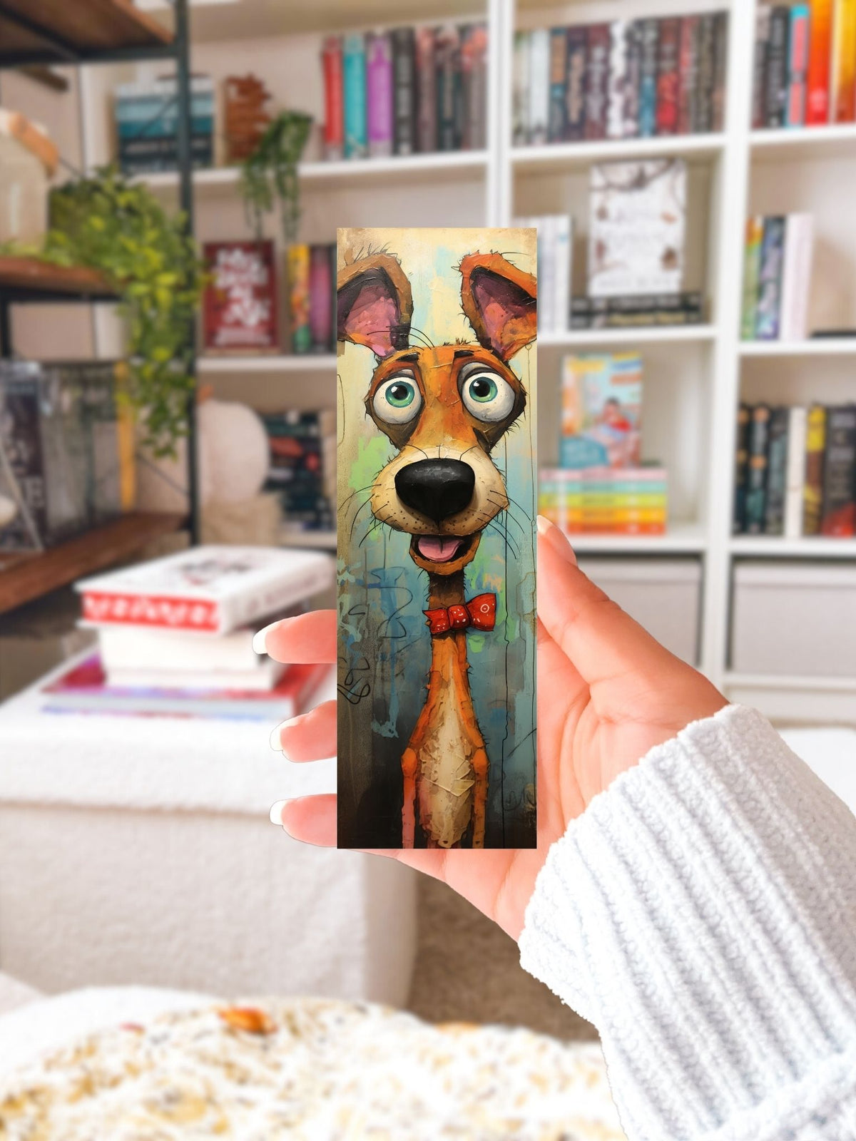 Hand houdt een boekenlegger met kleurrijke oranje hond, grote groene ogen en rood strikje vast voor een boekenkast.