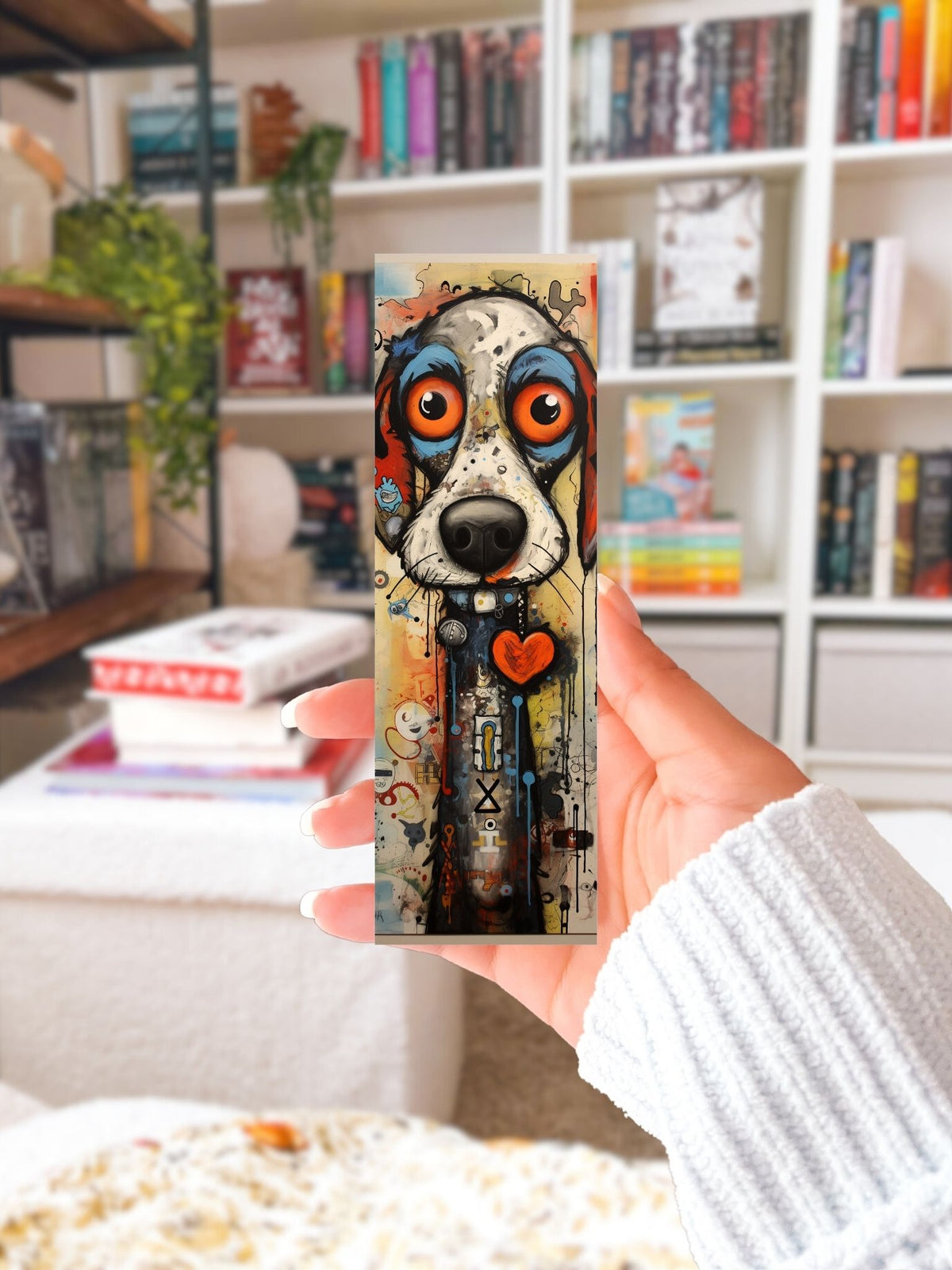 Hand houdt een lange boekenlegger met kleurrijke hond, grote oranje ogen en rood hartje voor een boekenkast.