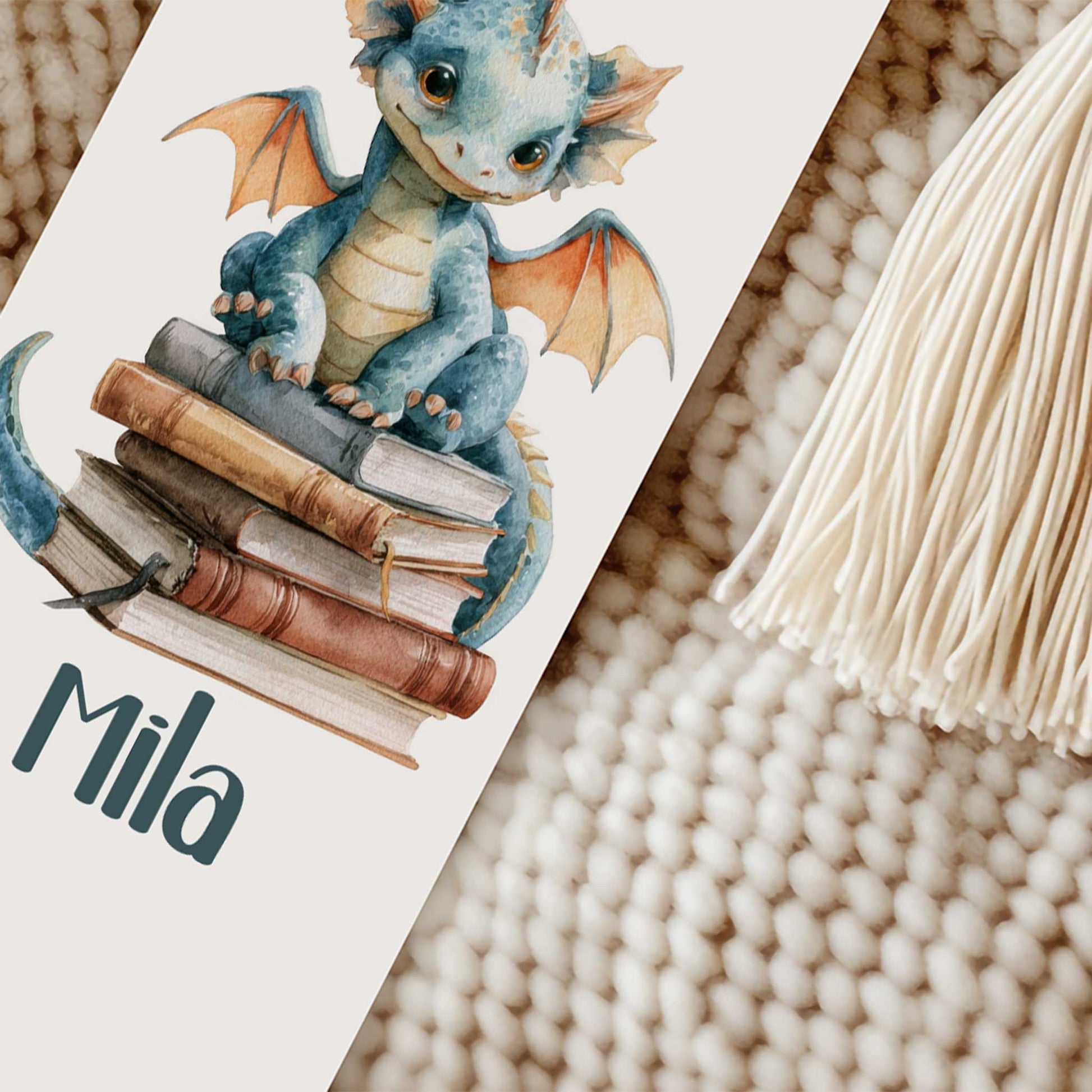 Close-up van een boekenlegger met een blauw draakje op een stapel boeken, de naam Mila en een crèmekleurig kwastje.