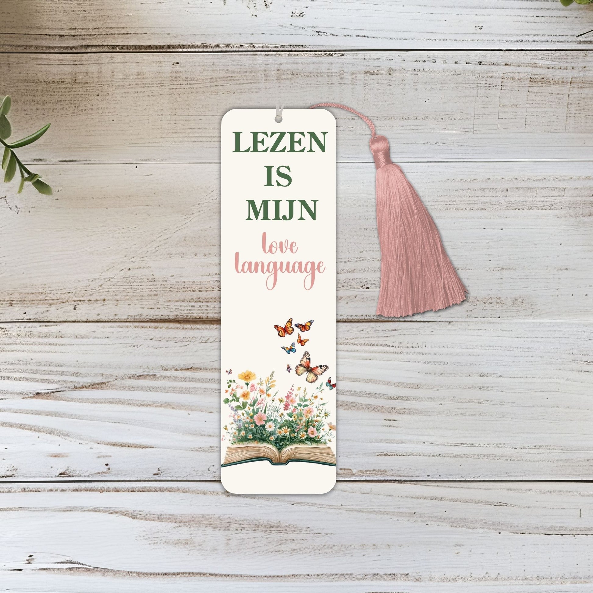 Boekenlegger met quote Lezen is mijn love language, open boek met bloemen en vlinders, roze suede kwastje, liggend op houten achtergrond