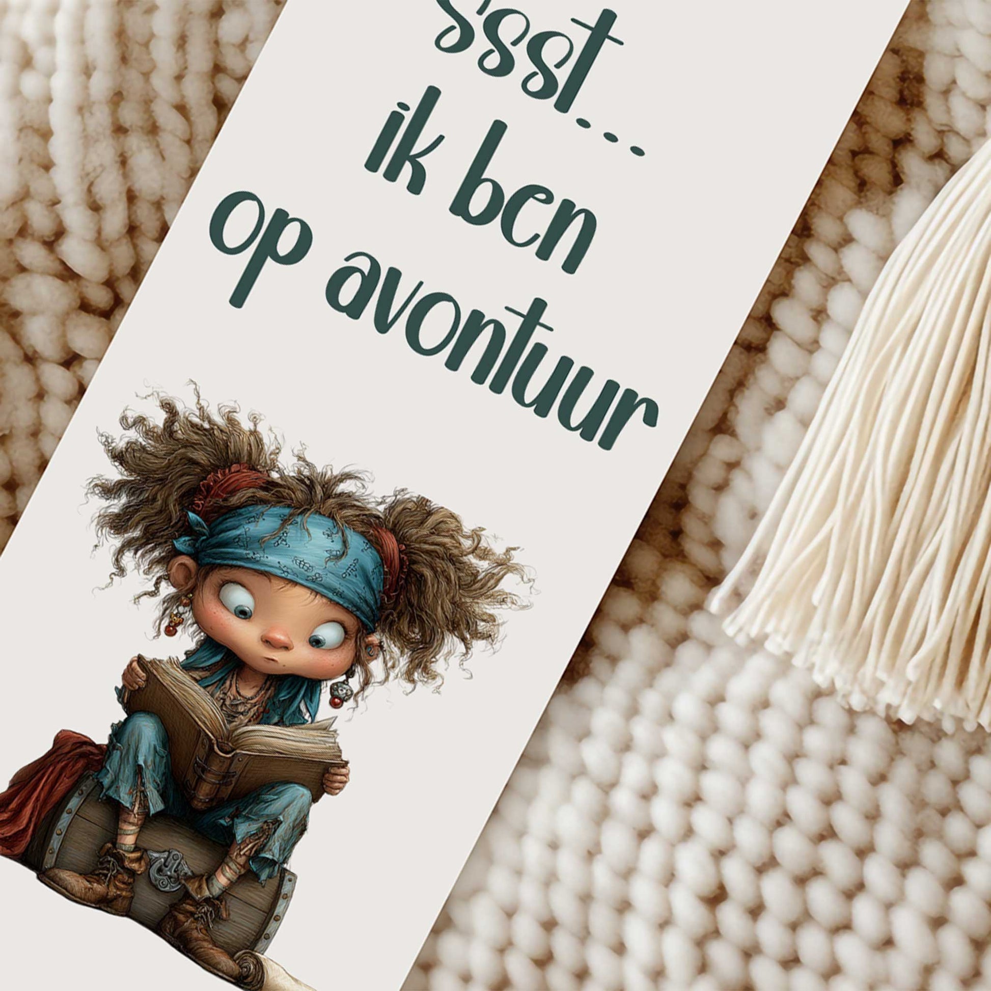 Close-up van een boekenlegger met de tekst 'Ssst... ik ben op avontuur', een lezend piratenkind op een schatkist en een crèmekleurig kwastje naast de boekenlegger.