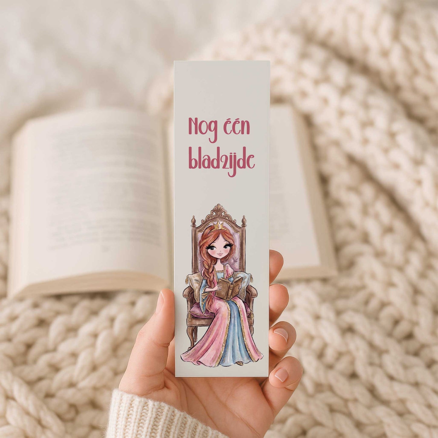 Hand houdt een boekenlegger vast met de tekst 'Nog één bladzijde' en een prinses die een boek leest op een sierlijke troon. Op de achtergrond ligt een open boek op een gebreide beige deken.