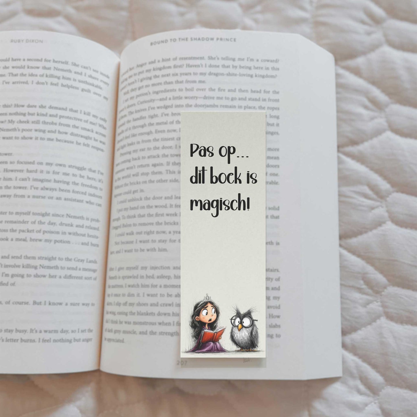 Boekenlegger met de tekst 'Pas op... dit boek is magisch!' en een illustratie van een prinses die een rood boek vasthoudt naast een uil. De boekenlegger ligt in een open boek.