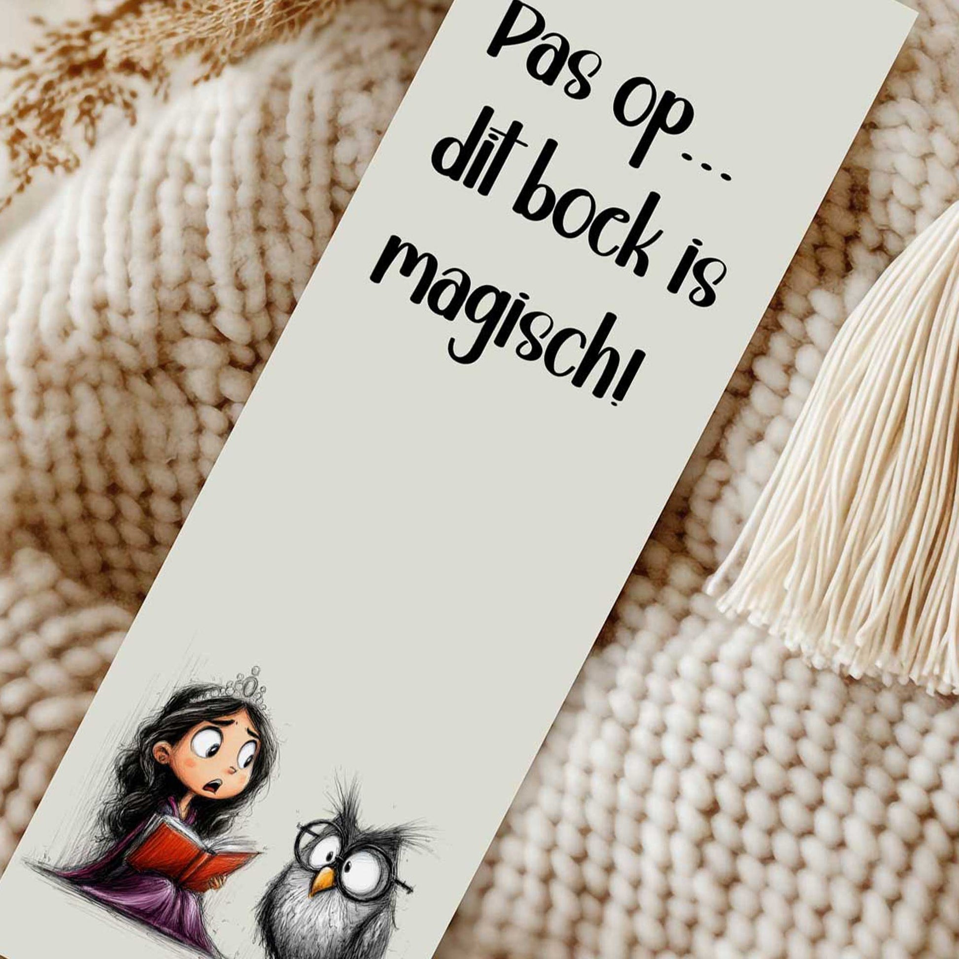Close-up van een boekenlegger met de tekst 'Pas op... dit boek is magisch!' en een prinses die een rood boek leest naast een uil. Naast de boekenlegger ligt een crèmekleurig kwastje.