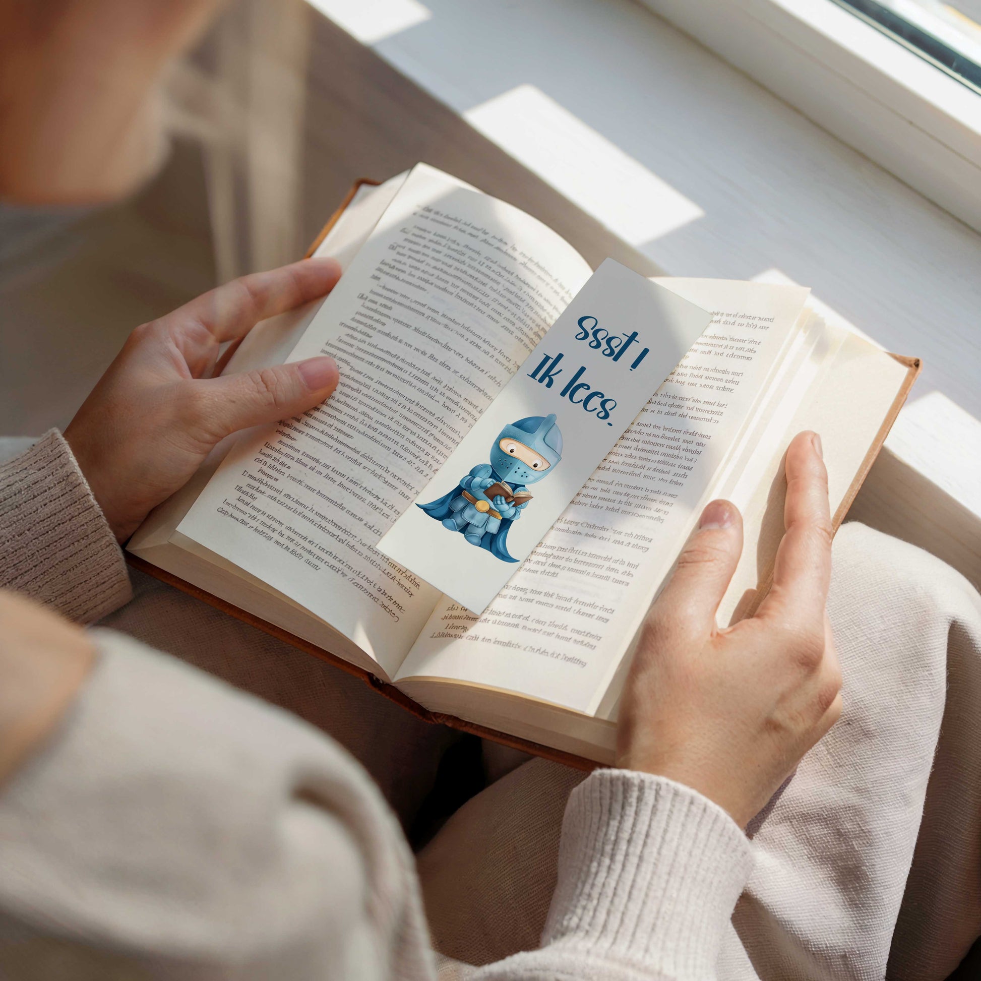 Sfeerfoto van een boekenlegger met een lezende blauwe ridder tussen de pagina's van een open boek.