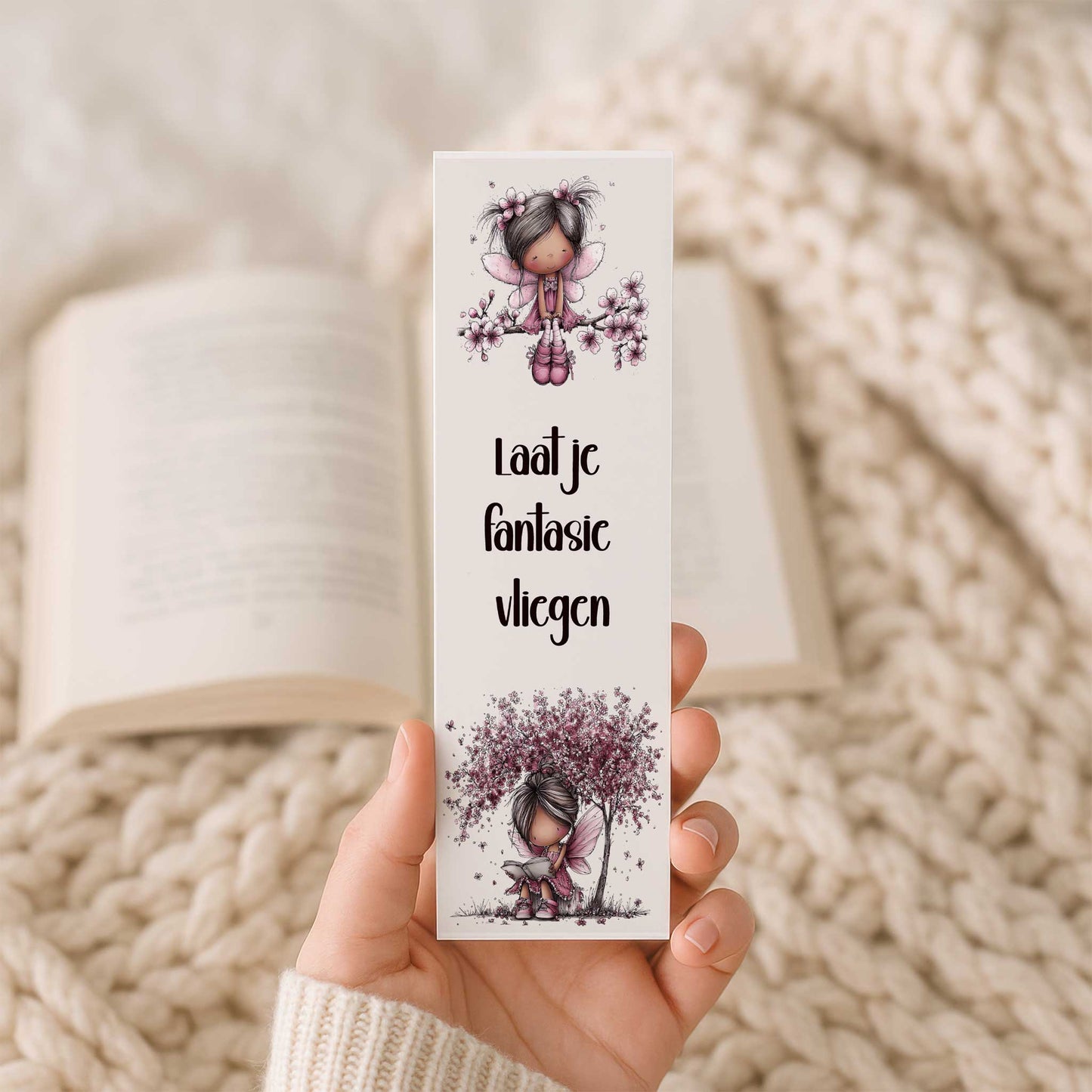 Hand houdt een boekenlegger met de tekst "Laat je fantasie vliegen", een vlinderfee op een bloesemtak en een lezende fee onder een bloeiende boom.