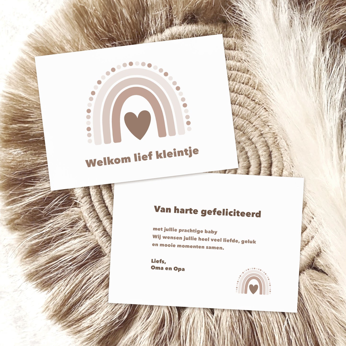 Twee witte cadeaukaartjes met regenboogprint in beige tinten op een zachte ronde ondergrond, waarbij op het bovenste kaartje de tekst “Welkom lief kleintje” staat en op het onderste kaartje een felicitatiebericht met de tekst “Van harte gefeliciteerd”