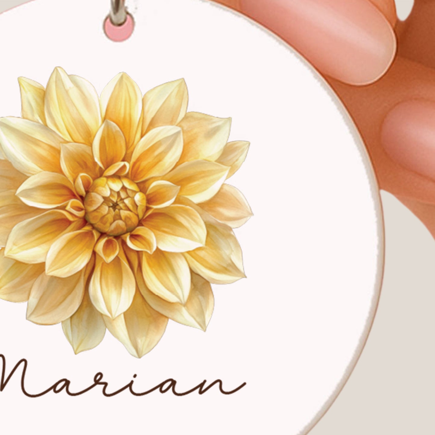 Close-up van een ronde sleutelhanger met een gele dahlia-illustratie en een gepersonaliseerde naam.