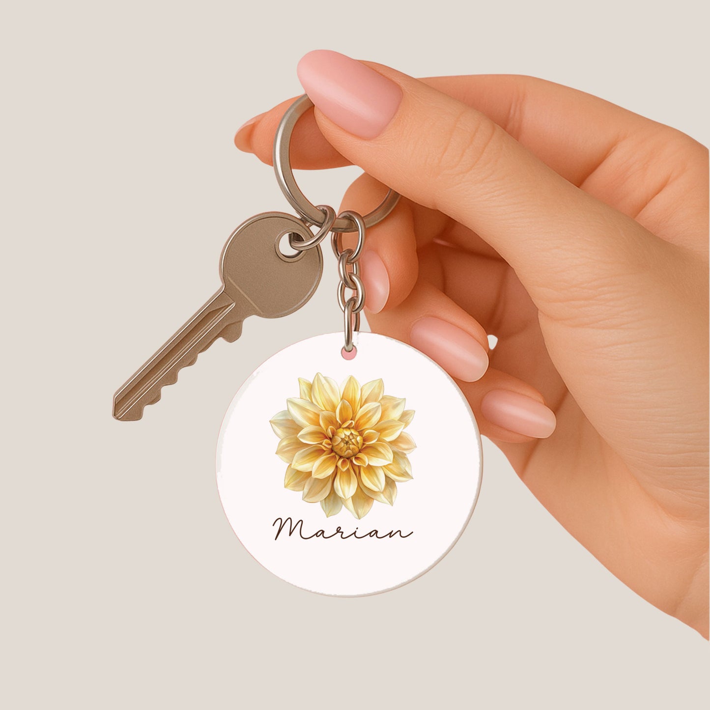 Hand houdt een ronde sleutelhanger met een dahlia-illustratiemet de naam marian vast