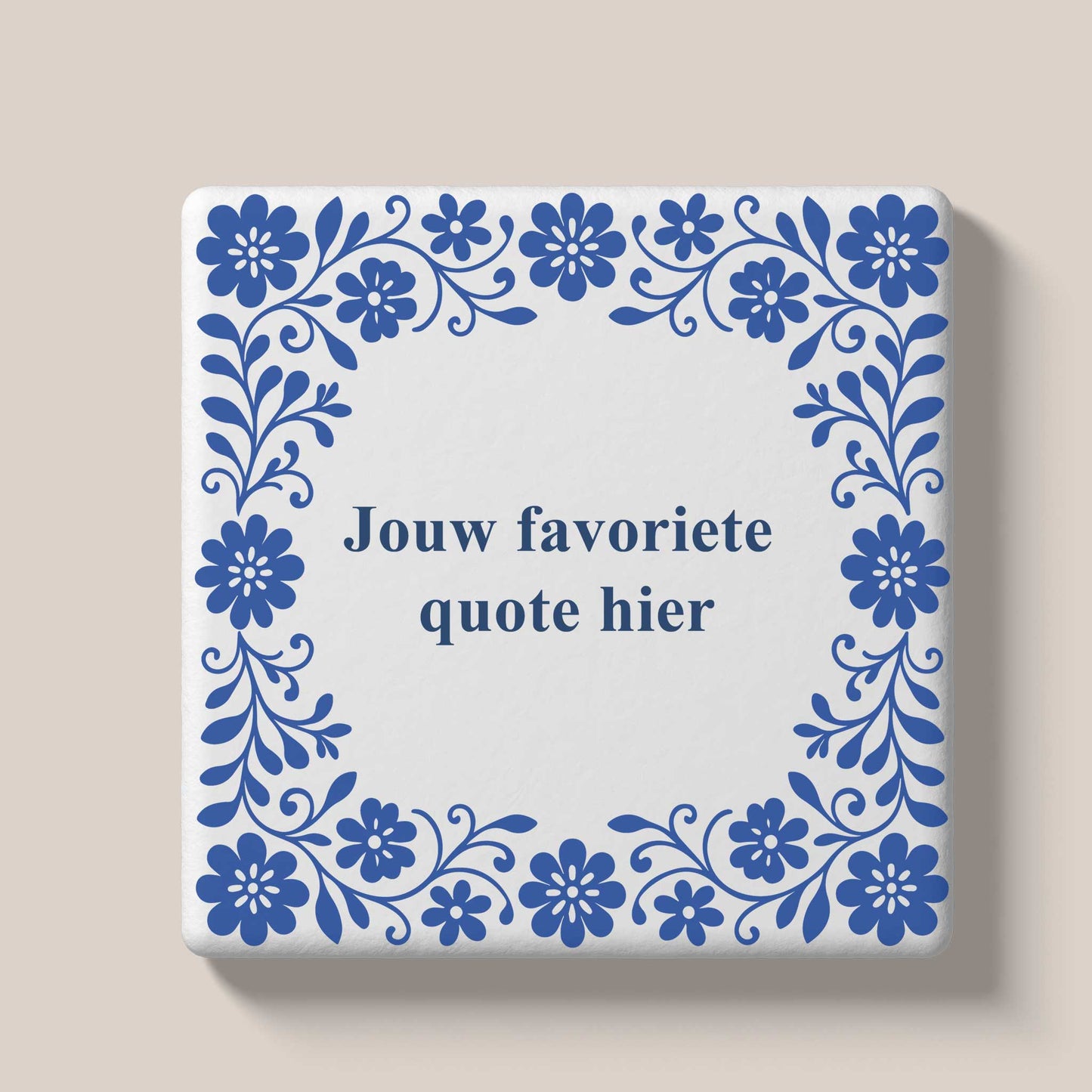 Delfts blauw keramisch tegeltje met sierlijke bloemenrand en de tekst 'Thuis is waar je verhaal begint' als voorbeeld van een gepersonaliseerd teksttegeltje