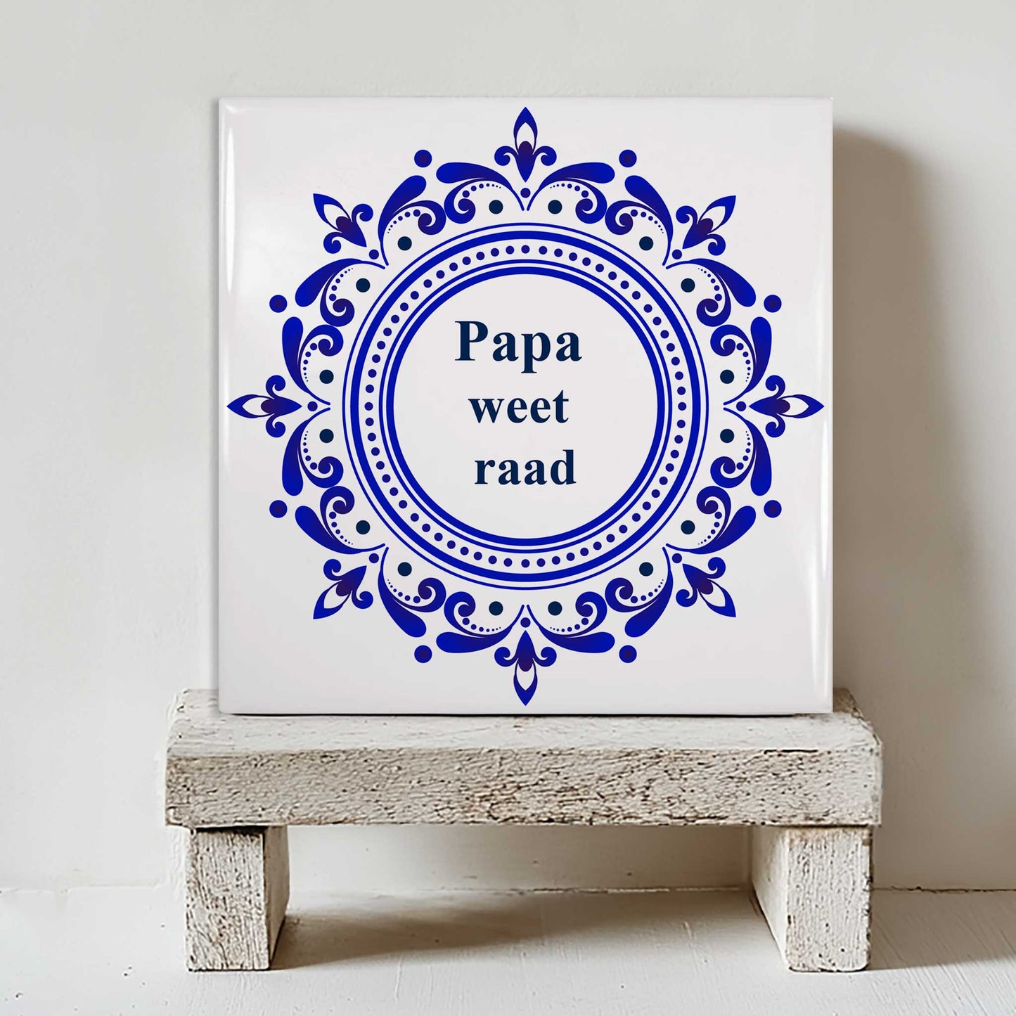 Delfts blauw tegeltje met klassieke ronde ornamenten en de tekst “Papa weet raad” op klein houten krukje