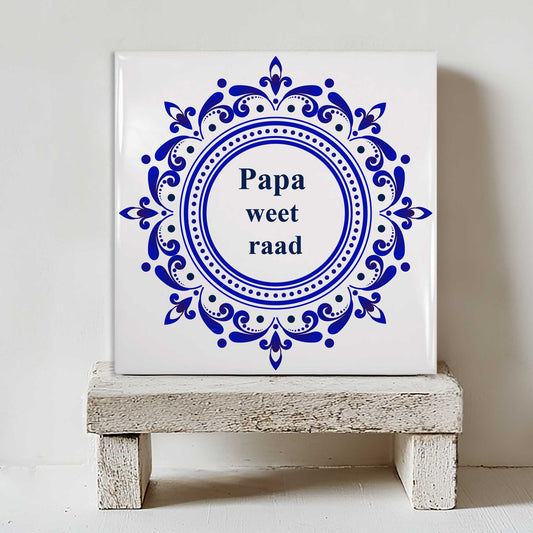 Delfts blauw tegeltje met klassieke ronde ornamenten en de tekst “Papa weet raad” op klein houten krukje