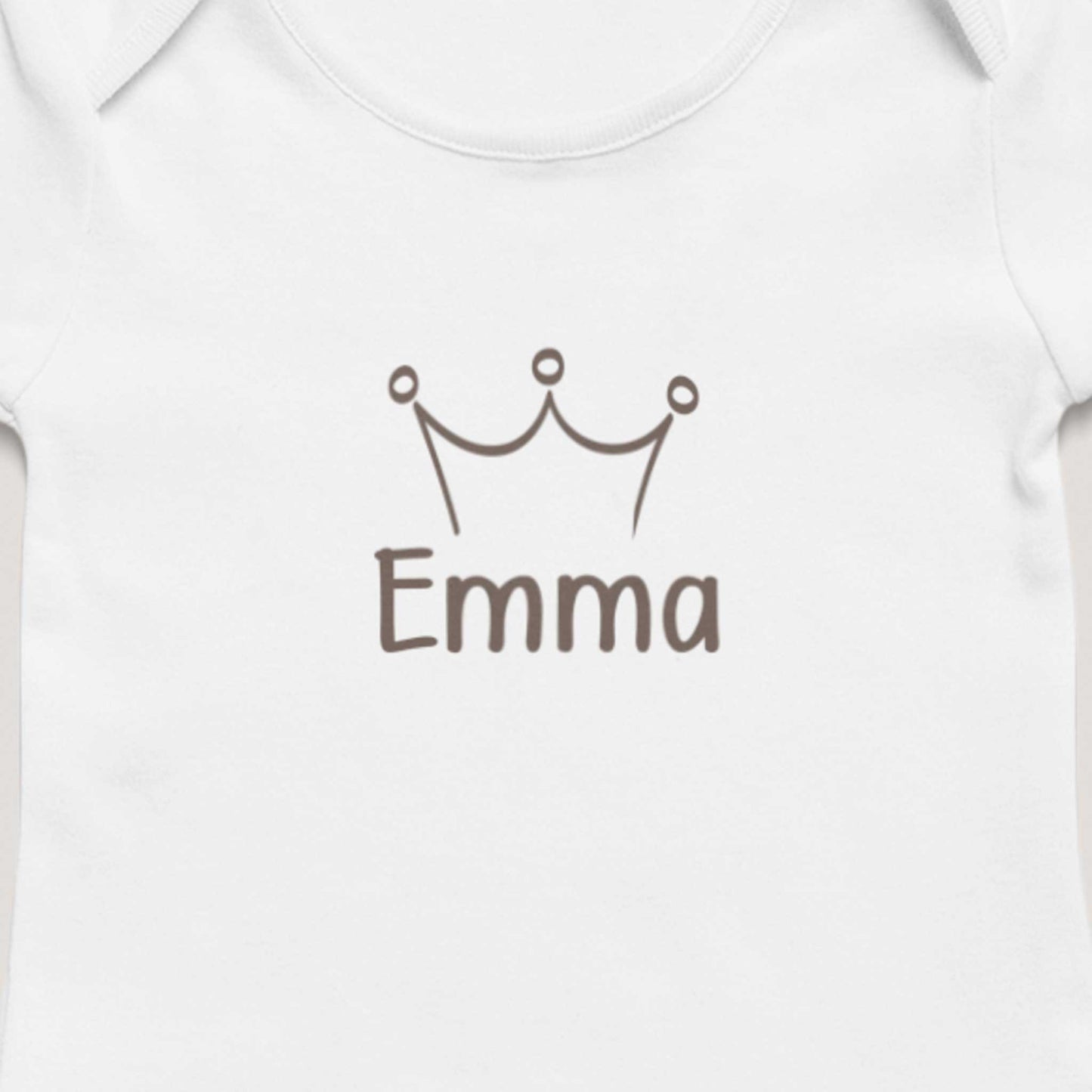 Close-up van wit gepersonaliseerd babyrompertje met taupekleurig kroontje en de naam Emma op zachte neutrale achtergrond.