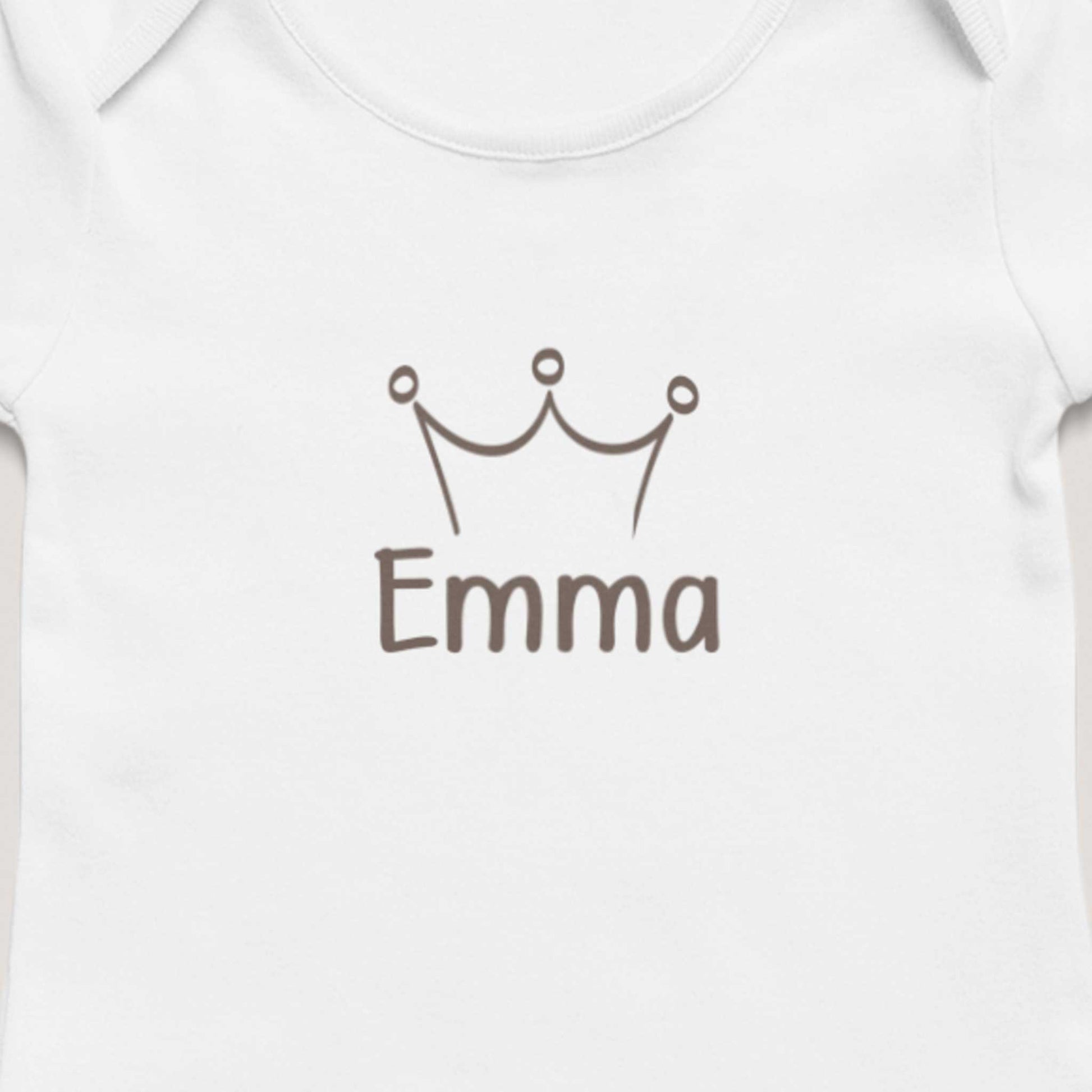 Close-up van wit gepersonaliseerd babyrompertje met taupekleurig kroontje en de naam Emma op zachte neutrale achtergrond.