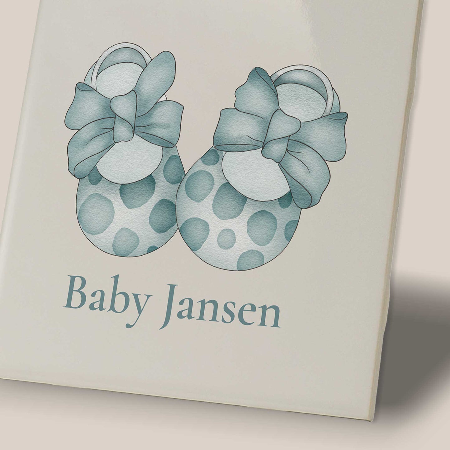 Detailfoto van keramisch baby tegeltje met blauwe babyschoentjes illustratie en naam Baby Jansen zichtbaar op de voorkant.