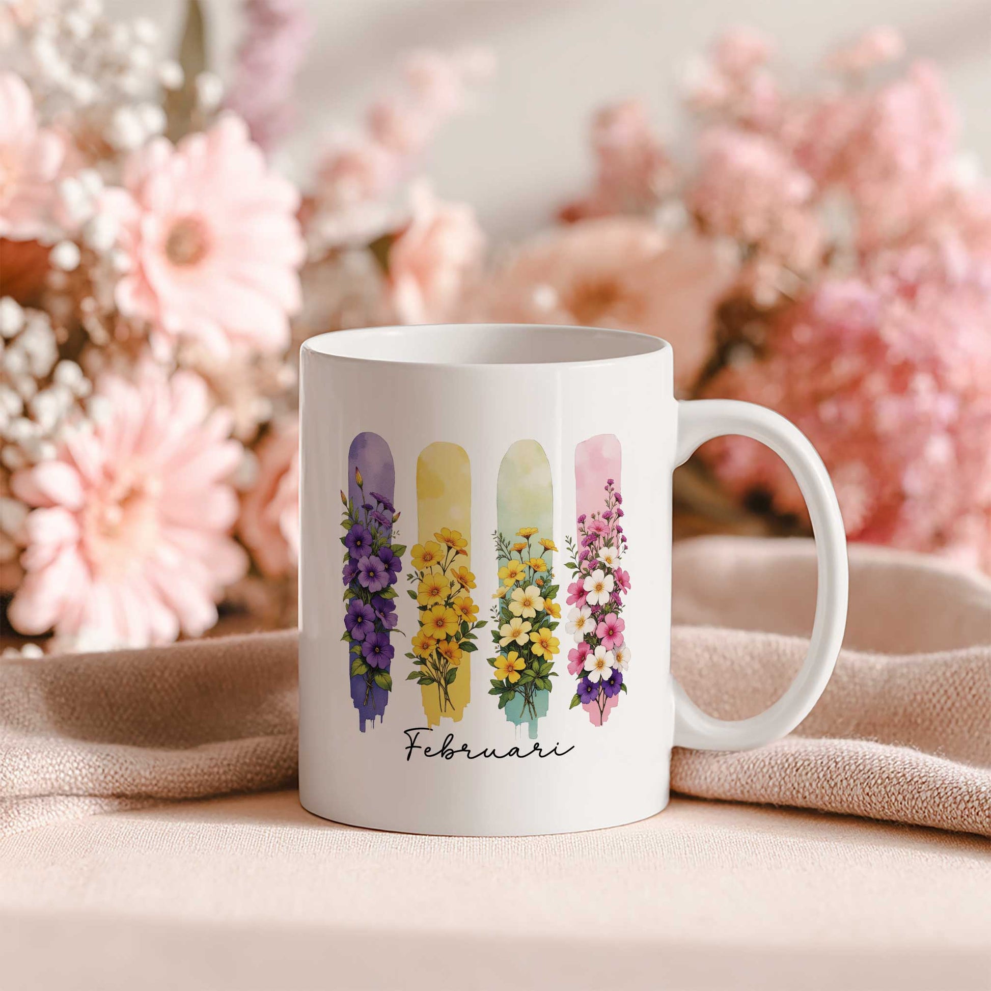 Witte mok met de geboortebloemen van februari in brush effect op een beige doek, met een achtergrond vol roze bloemen.