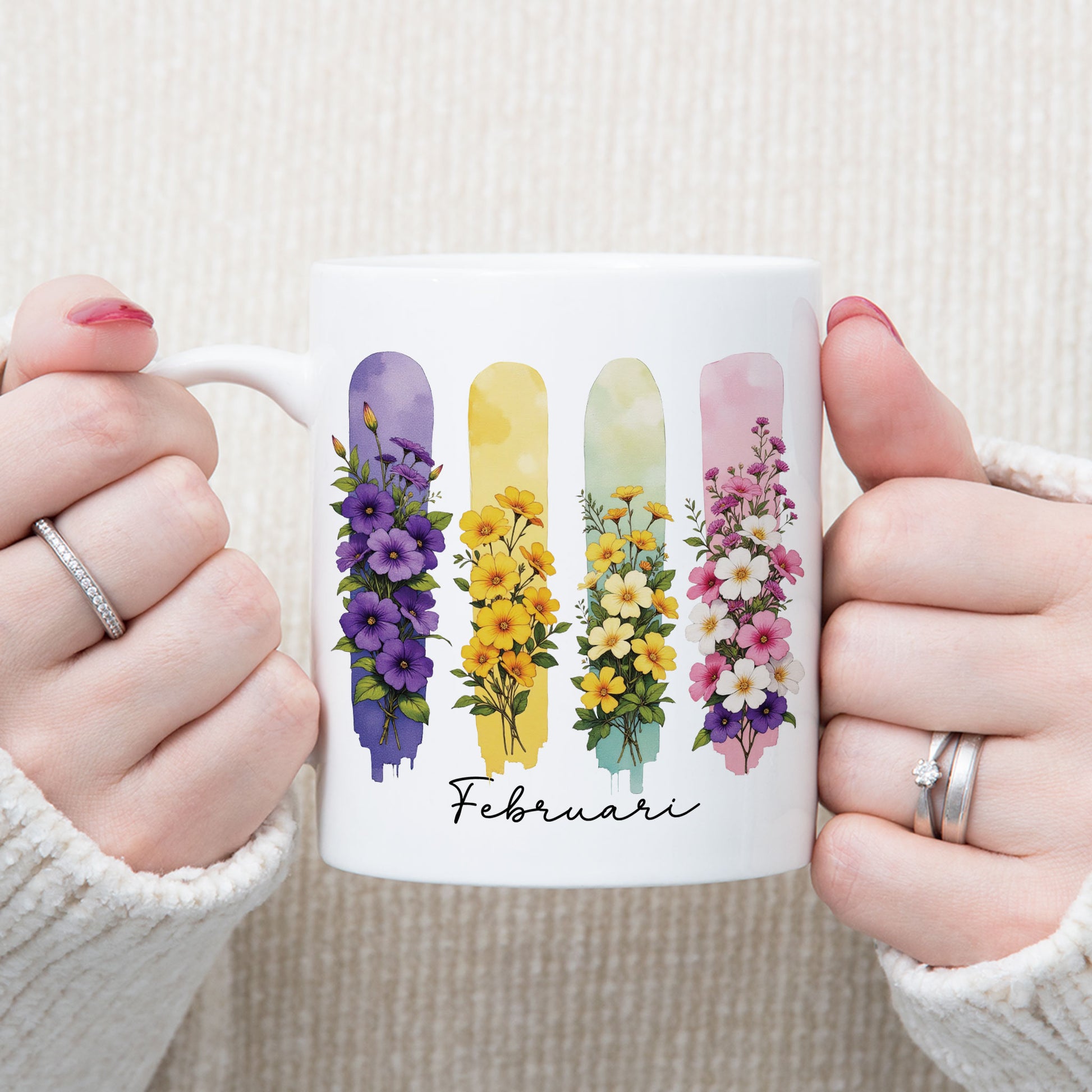 Persoon houdt een witte mok met de geboortebloemen van februari in brush effect met beide handen vast, waarbij het bloemenontwerp goed zichtbaar is.