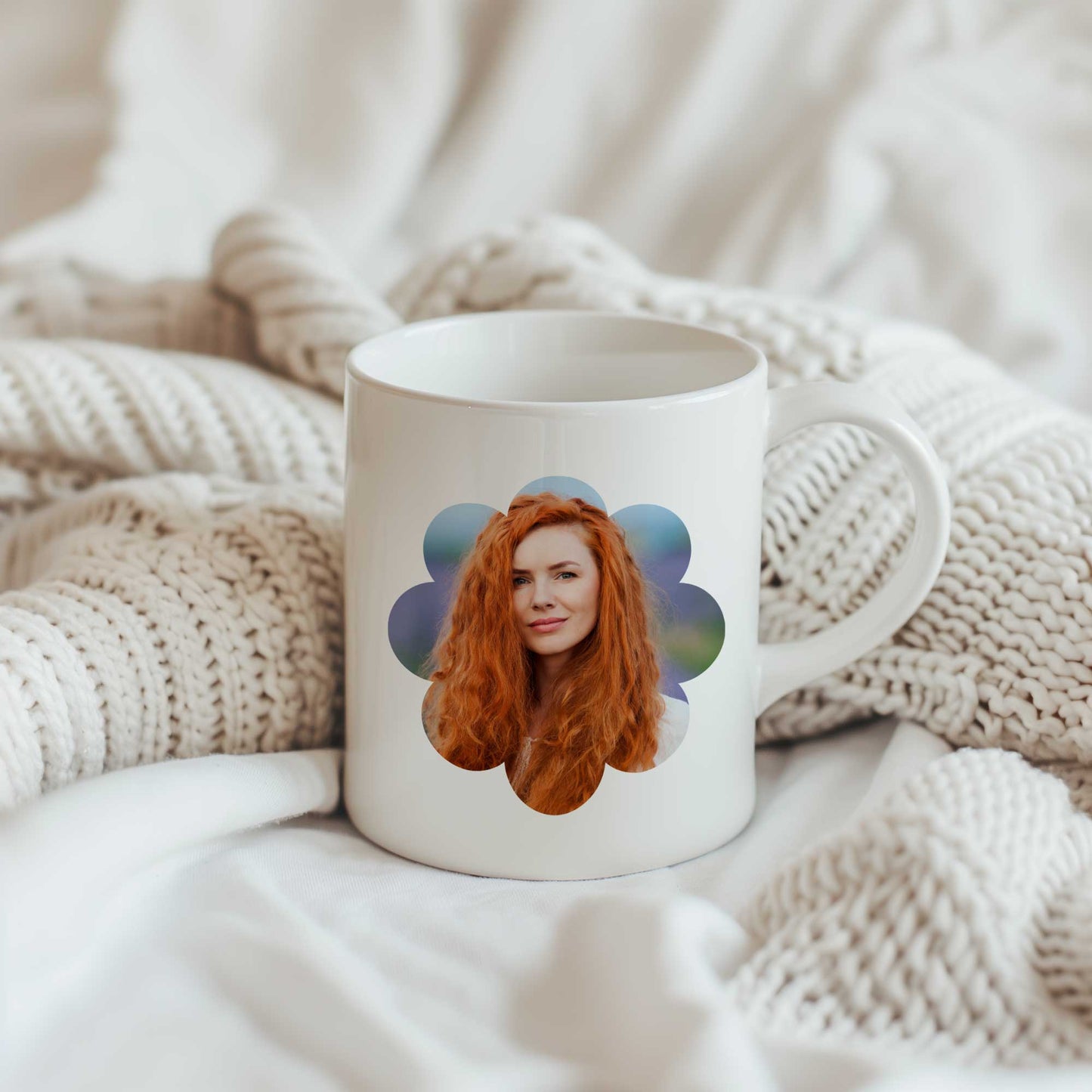 Witte keramische fotomok met een portret van een roodharige vrouw in een bloemvormig fotokader, geplaatst op een zachte beige gebreide deken.