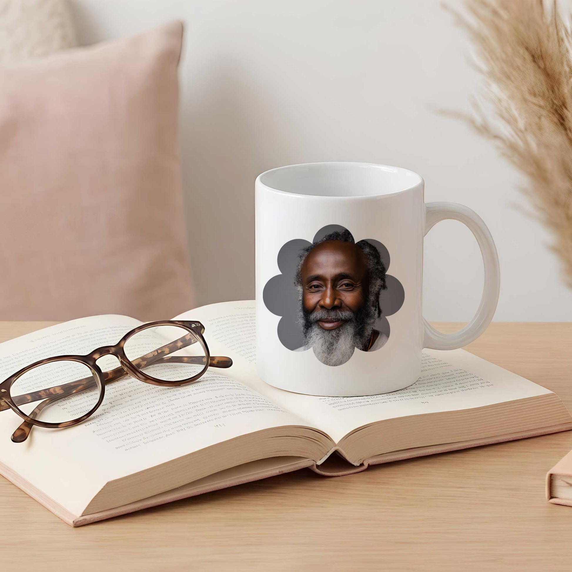 Witte keramische fotomok met een portret van een oudere man in een bloemvormig fotokader, geplaatst op een open boek met een leesbril op een lichte houten tafel.