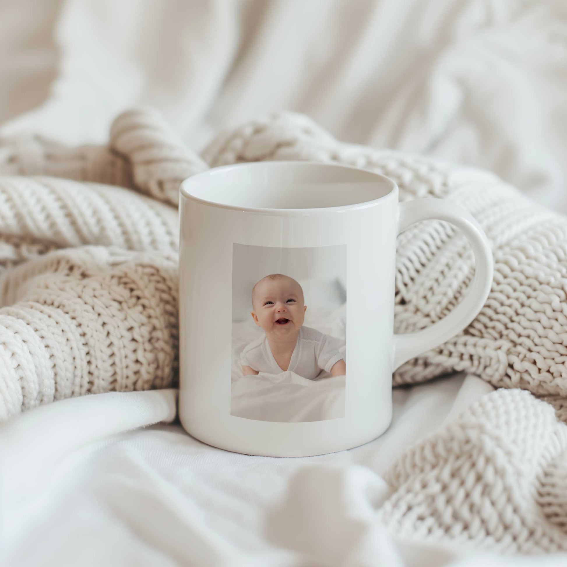 Witte keramische mok met rechthoekige babyfoto op een beige gebreide deken