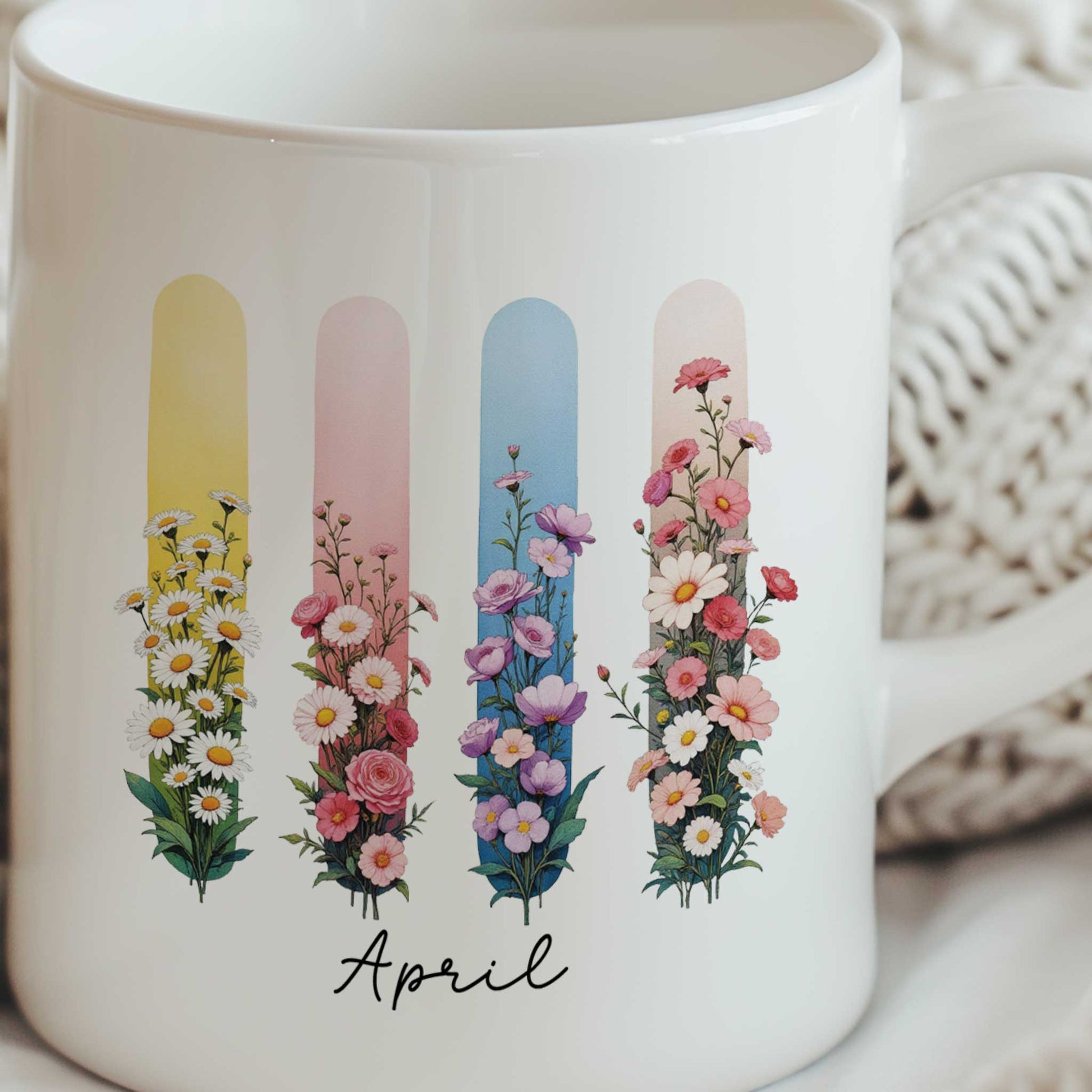Close-up van een witte mok met illustratie van madeliefjes en lathyrus in een kleurrijk brush effect. De mok wordt met beide handen vastgehouden door een persoon in een witte gebreide trui tegen een lichtbeige geribbelde achtergrond.