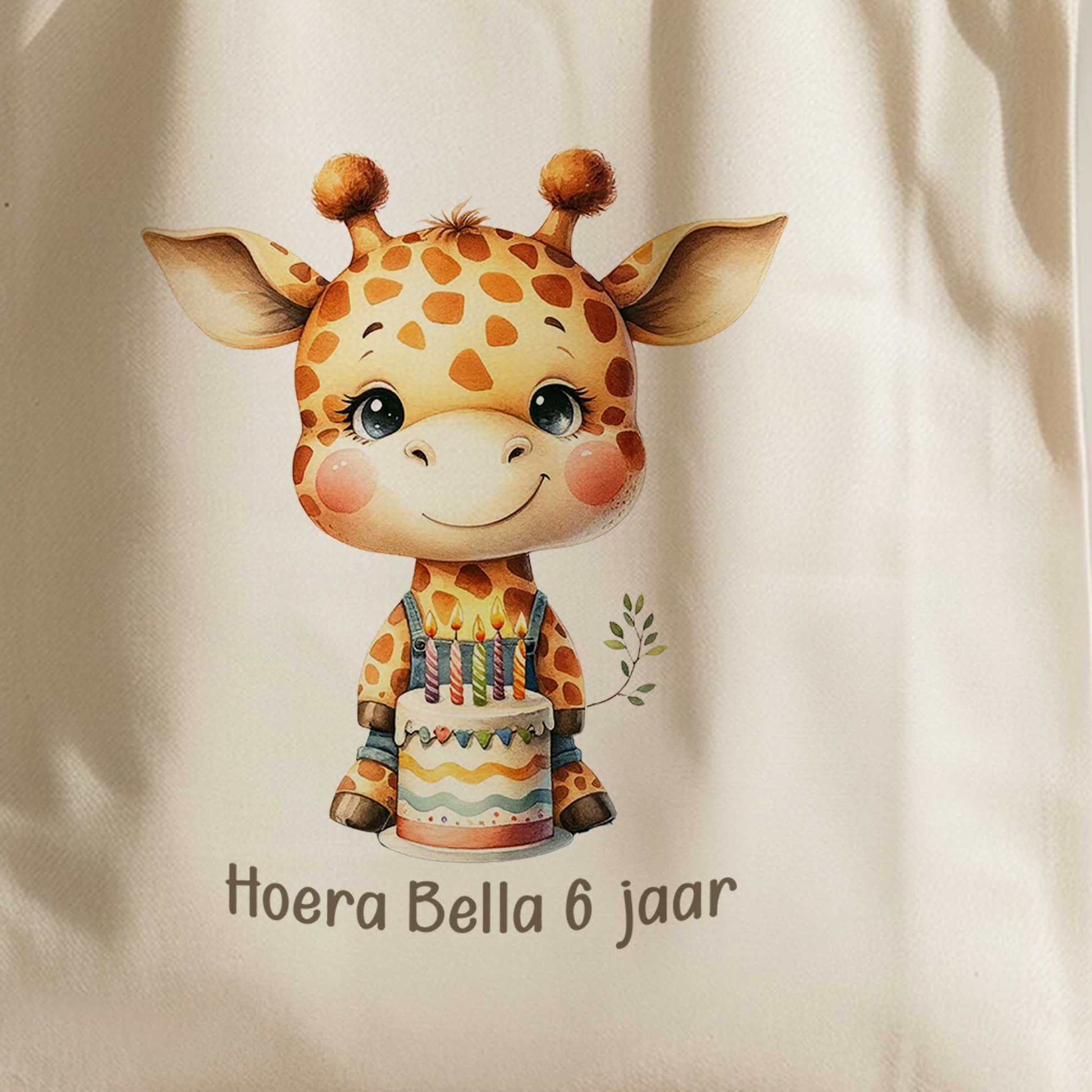 Close-up van de bedrukking op een gepersonaliseerde totebag met een schattige giraf, verjaardagstaart en de tekst 'Hoera Bella 6 jaar'.