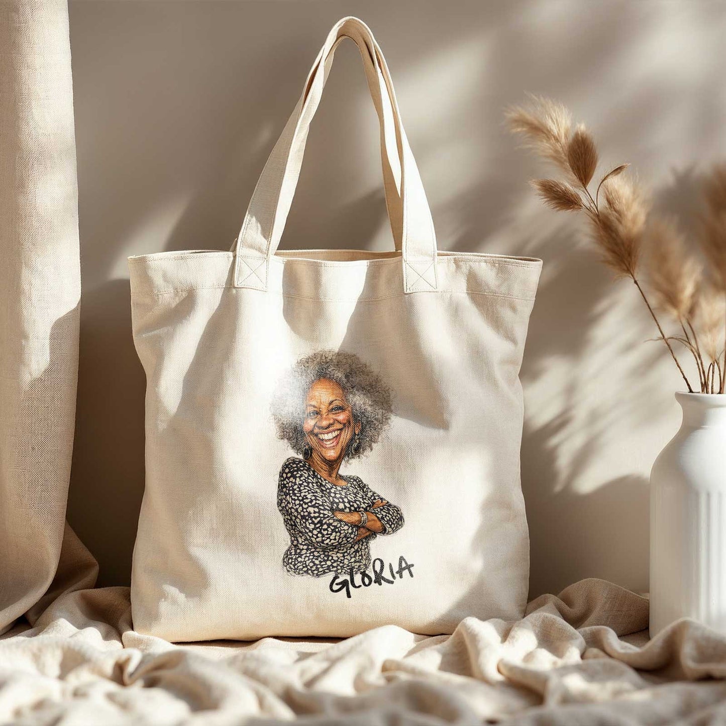Beige katoenen totebag met gepersonaliseerde karikatuur van een oudere vrouw met grijs krullend haar en de naam Gloria, gefotografeerd in warm beige interieur met droogbloemen en zacht zonlicht.