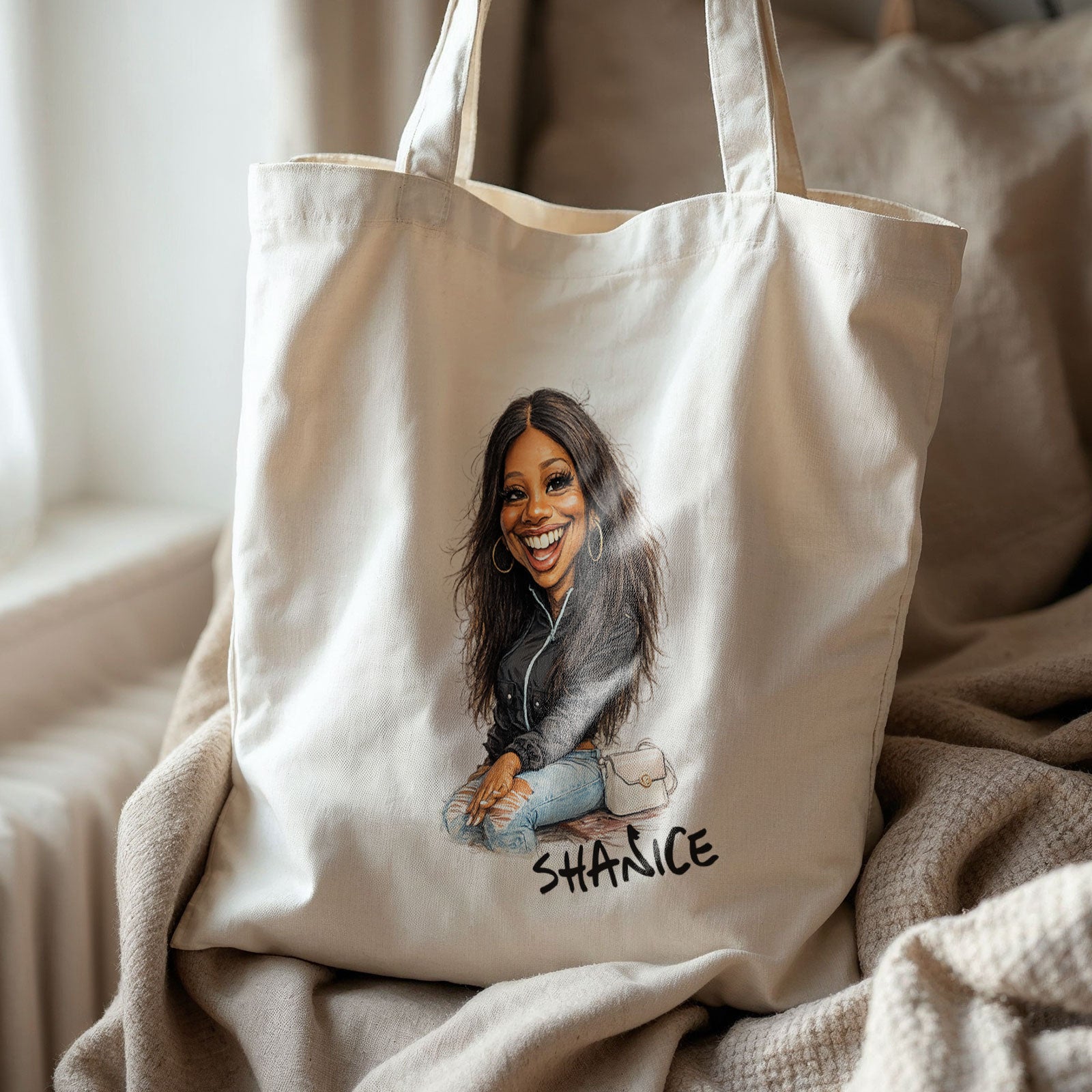 Beige katoenen totebag met gepersonaliseerde karikatuur van een jonge vrouw en de naam Shanice, geplaatst op zachte beige dekens in warm interieurlicht.