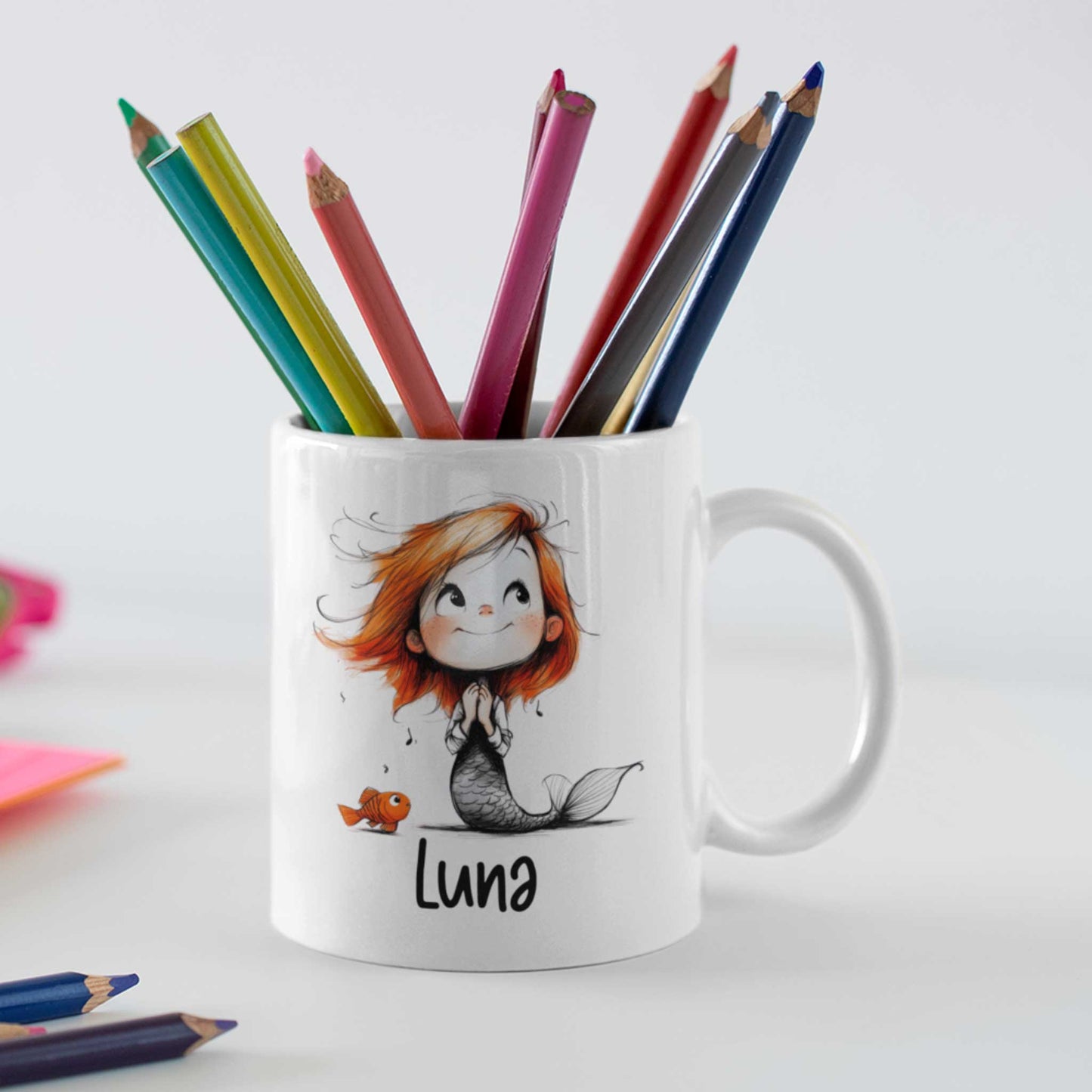 Witte keramische mok gevuld met kleurpotloden, bedrukt met een schattige zeemeermin met oranje haar, een klein visje en de naam Luna.
