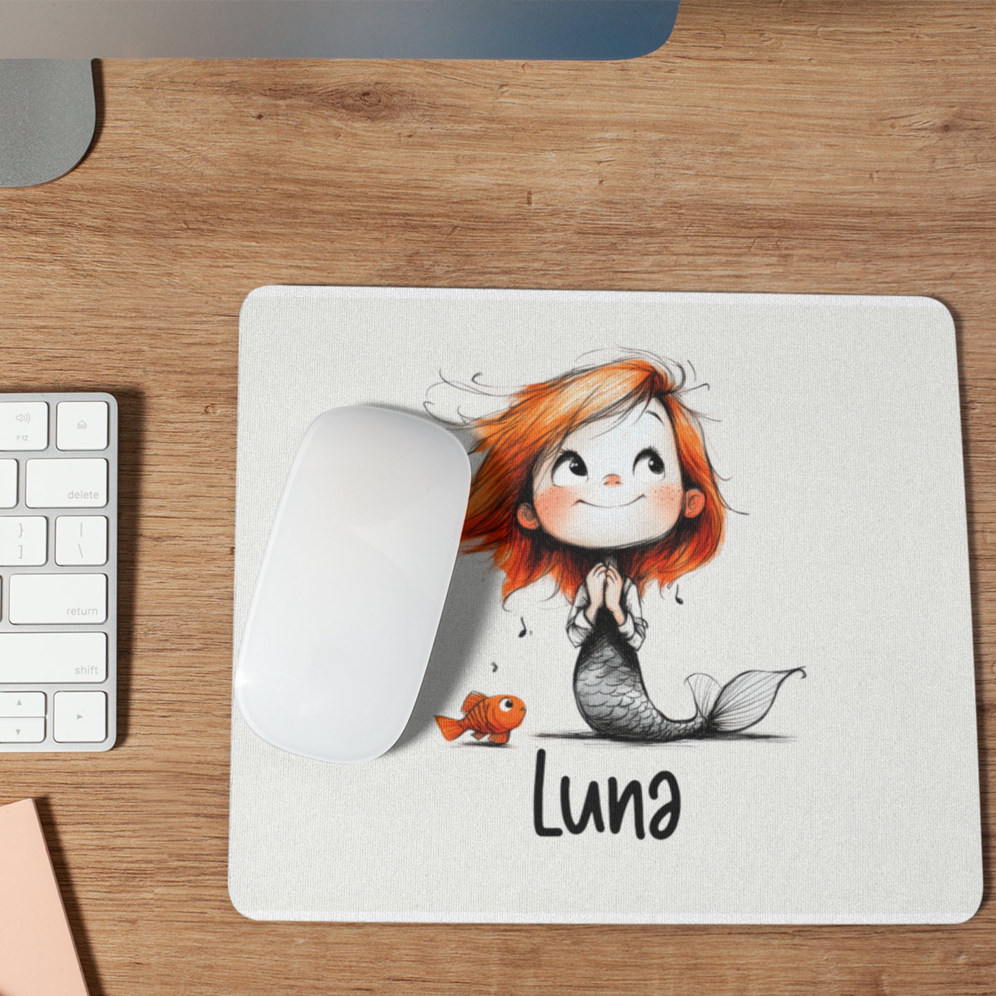 Gepersonaliseerde witte muismat met een schattige zeemeermin met oranje haar, een klein visje en de naam Luna op een houten bureau naast een computermuis.