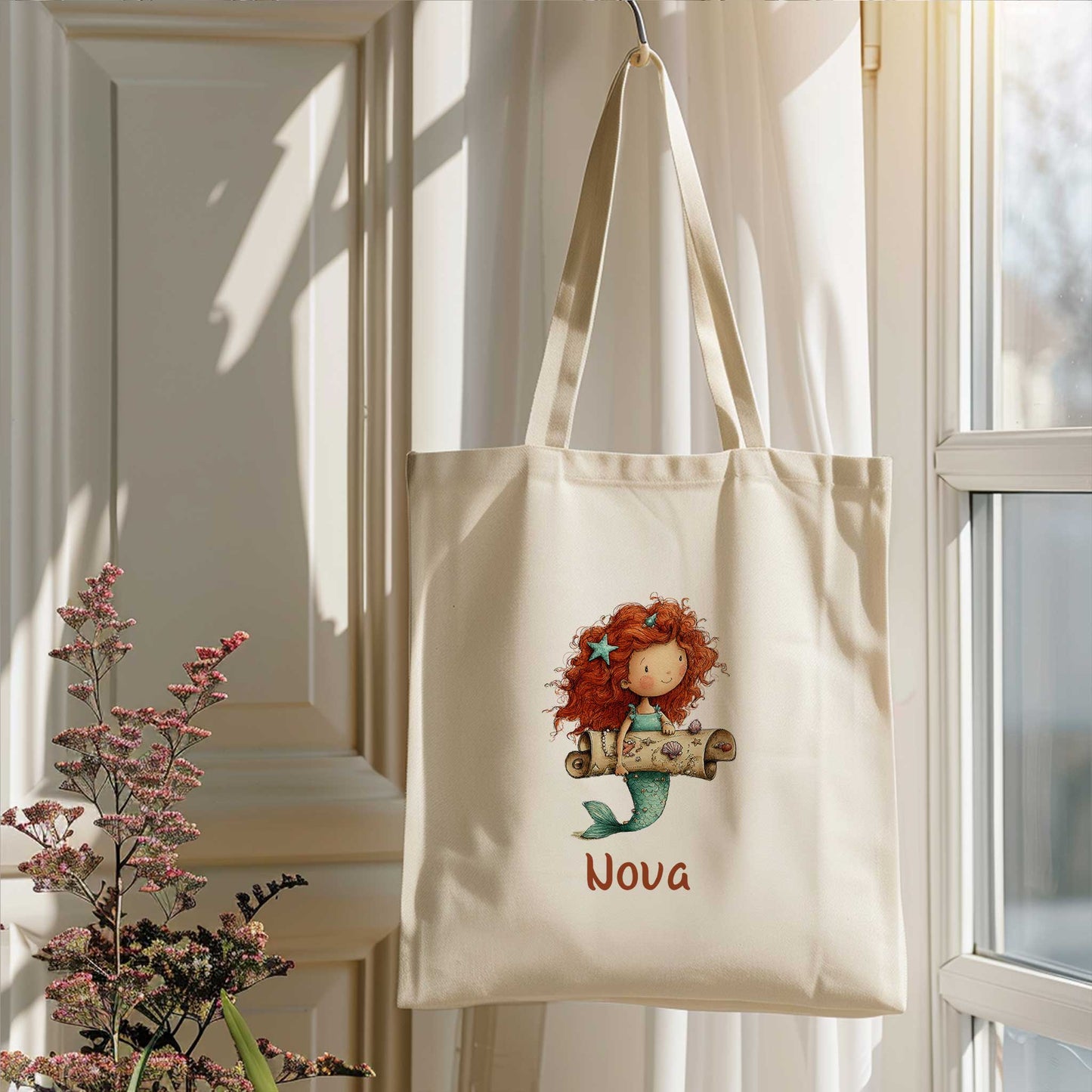 Zeemeermin totebag met naam Nova hangend bij een raam in zacht daglicht met bloemen op de voorgrond.