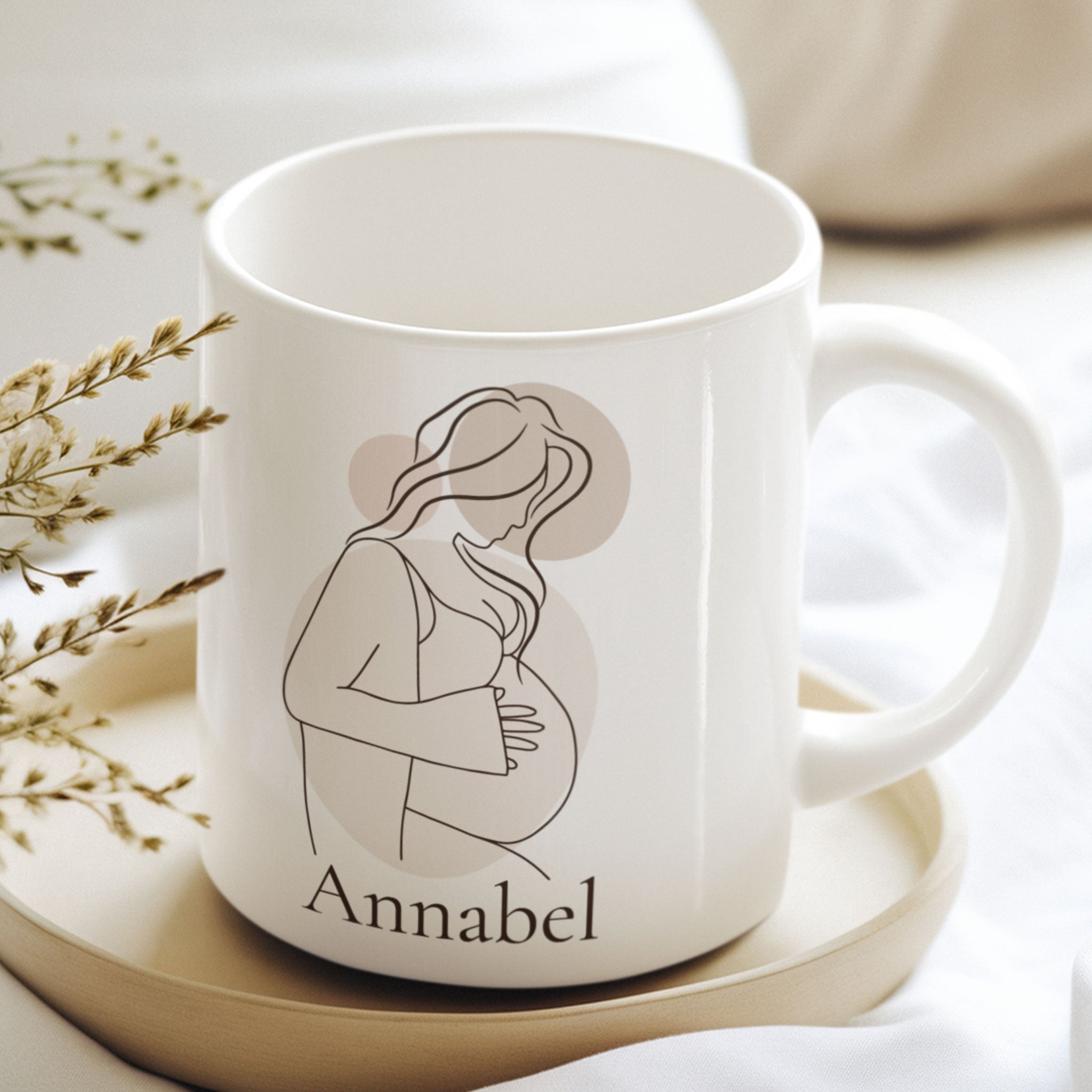 Gepersonaliseerde zwangerschapsmok met naam Annabel op een houten schaaltje tussen droogbloemen in zachte neutrale kleuren. Minimalistische mok met lijntekening van een zwangere vrouw.