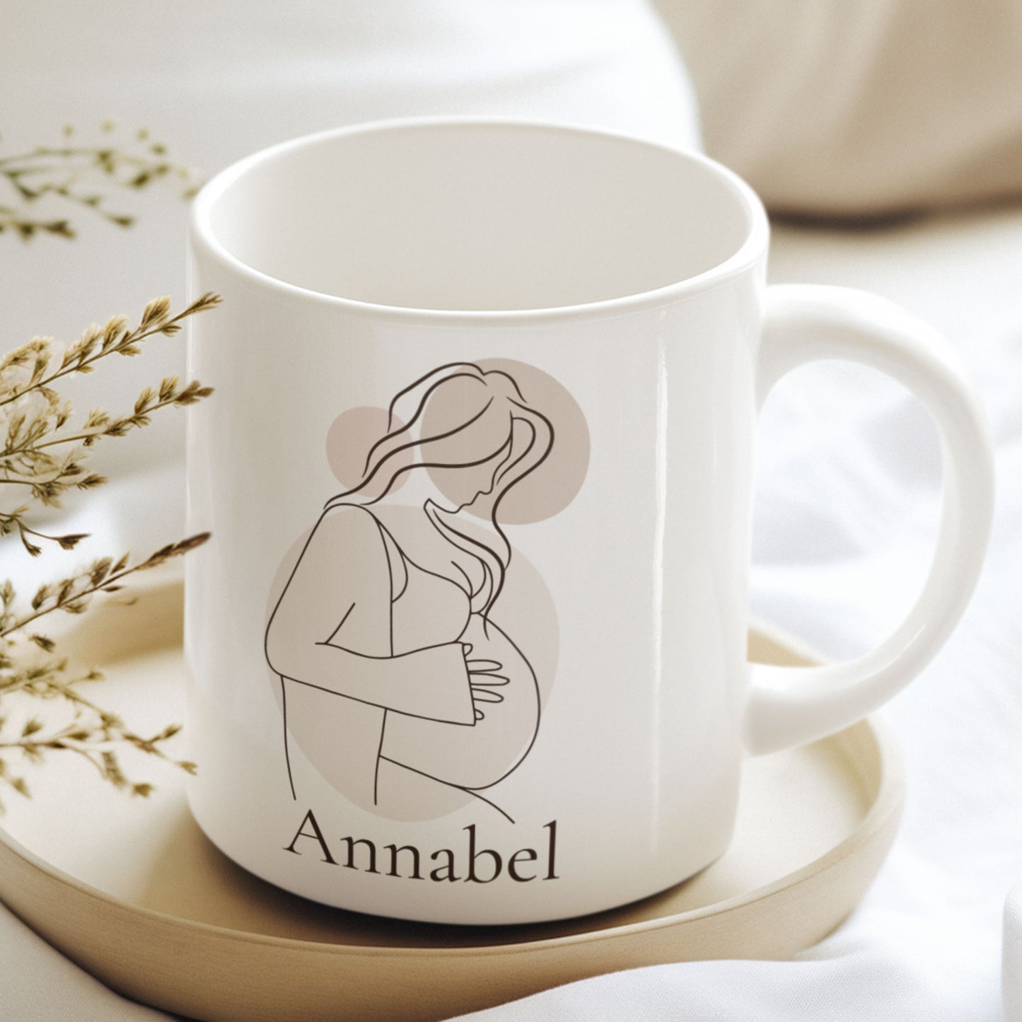 Gepersonaliseerde zwangerschapsmok met naam Annabel op een houten schaaltje tussen droogbloemen in zachte neutrale kleuren. Minimalistische mok met lijntekening van een zwangere vrouw.