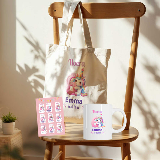 Giftset unicorn verjaardag met totebag, mok en stickervel met tekst ‘Hoera Emma is 6 jaar’ op houten stoel in zonlicht