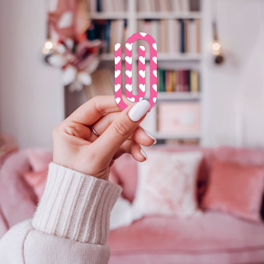 Hand houdt een roze jumbo paperclip met hartjes vast