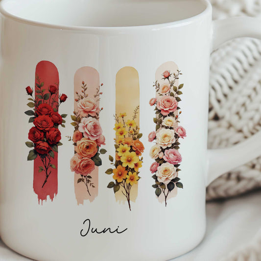 Close-up van een witte mok met de geboortebloemen van juni op een zachte gebreide deken.