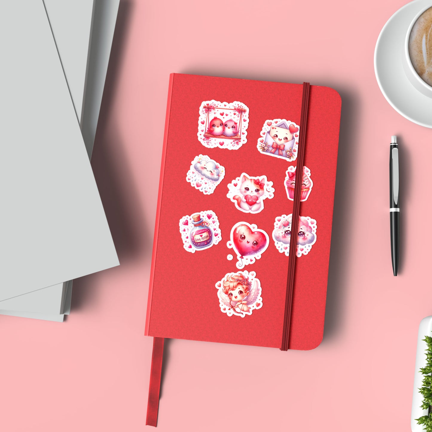 Rood notitieboek versierd met 9 geplakte stickers uit het Sweet Love stickervel, liggend op roze ondergrond met pen, koffie en tijdschriften ernaast